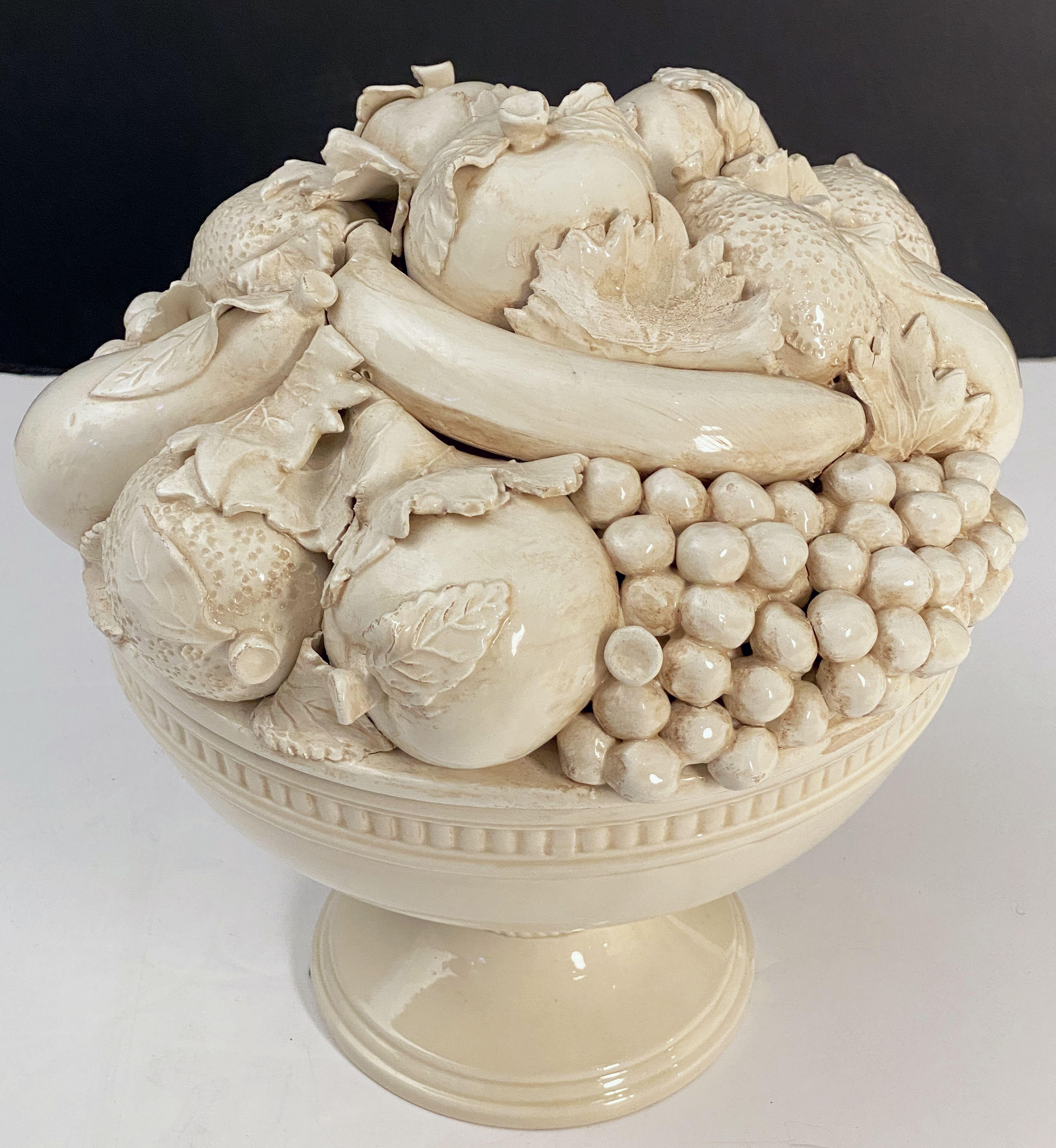 A fine large Italian cream-ware or white glazed ceramic pedestal bowl with mixed fruit topiary top, featuring a fitted lid with a relief of mixed fruits around the circumference, over a lower body with bowl and pedestal support on a round plinth