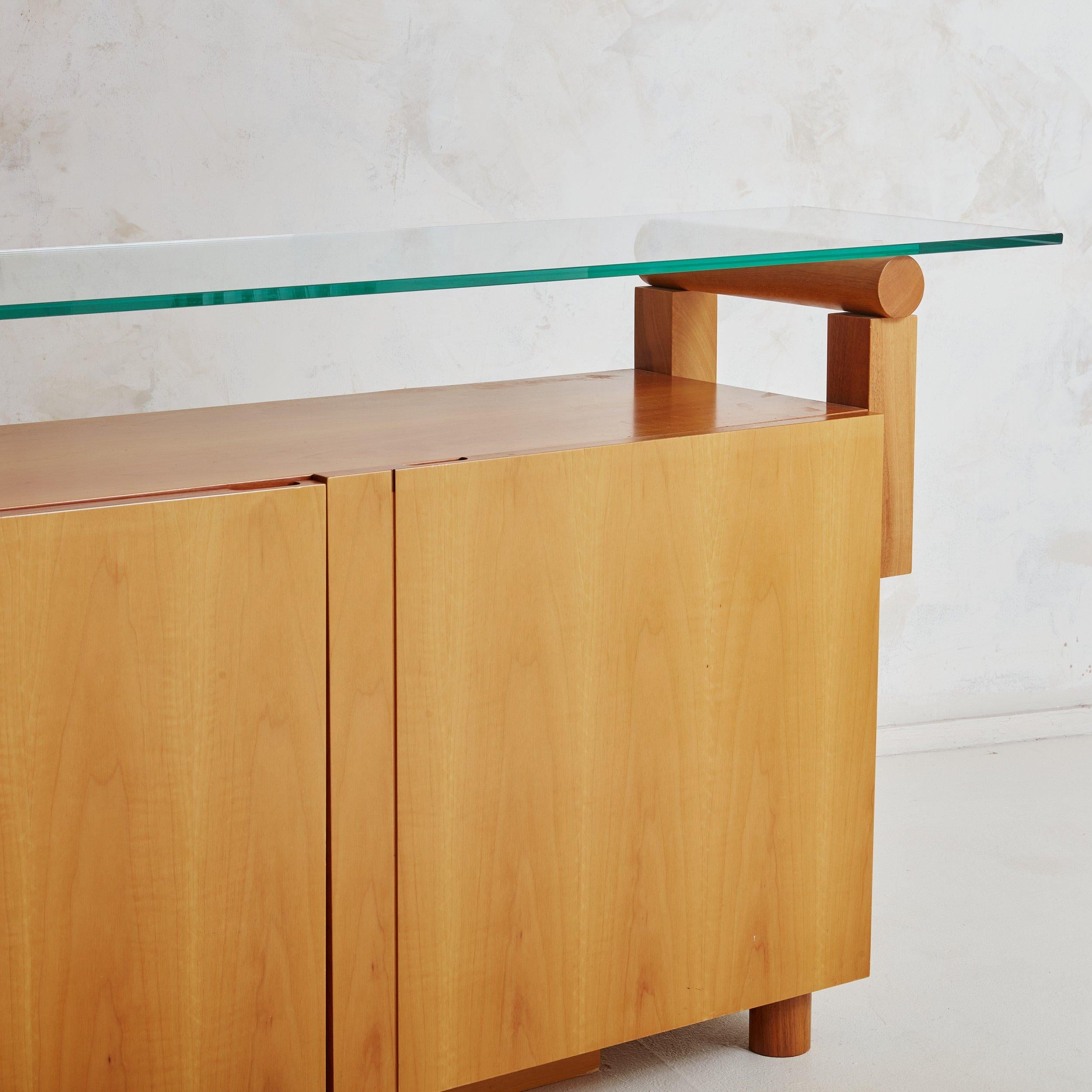 A Mid-Century Modern wood and glass shelf credenza from the 1980s. The monumental scale of this credenza is rare, featuring four flat paneled doors that reveal two shelves and separate storage spaces. The honey tinged wood has a slight sheen with