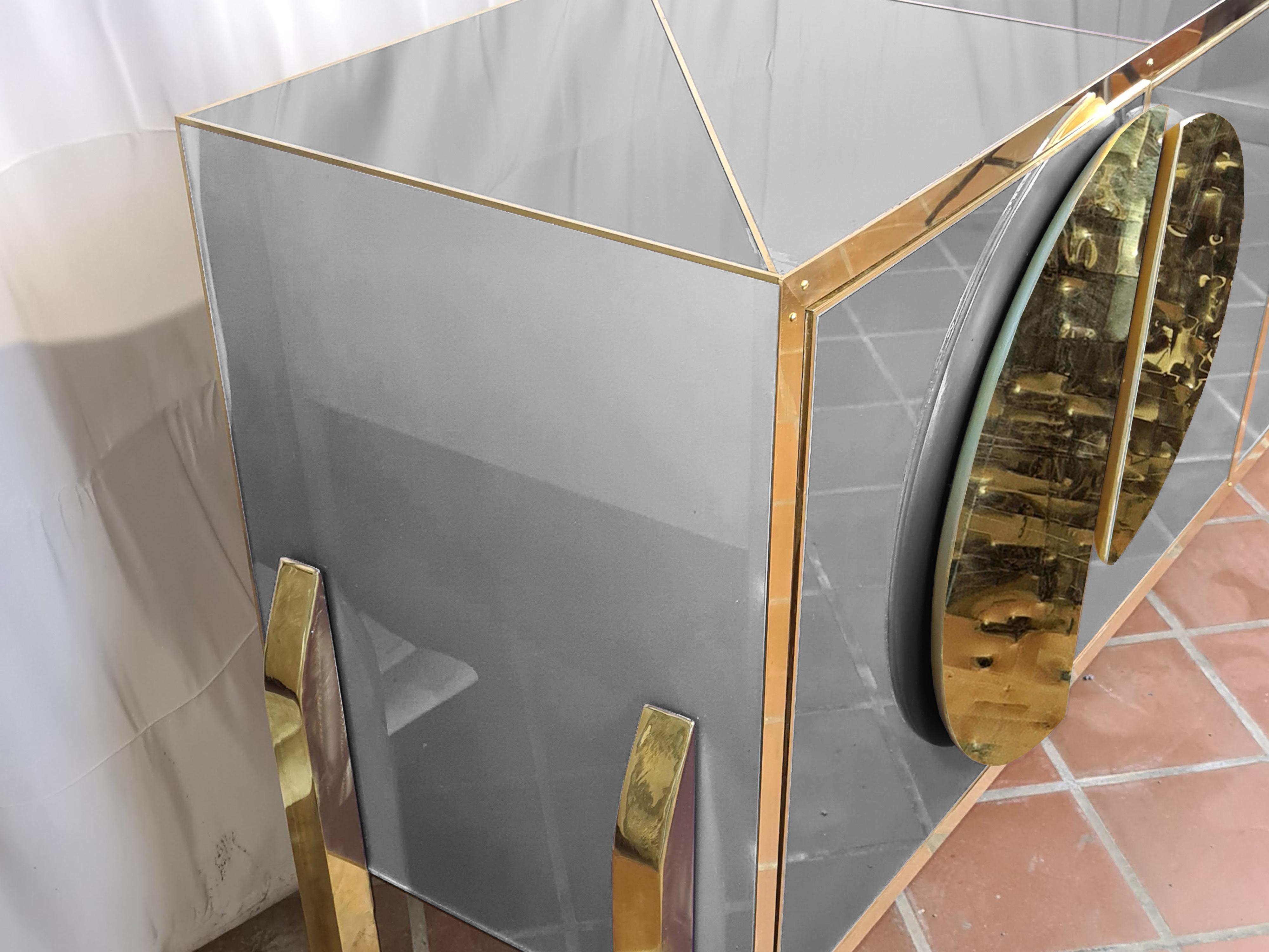 Handcrafted in Italy, it features an elegant birch frame embellished with beautiful grey Murano glass elements and elegant brass handles. 

Bevelled glass surfaces add depth and sophistication, while the innovative geometric design of the doors