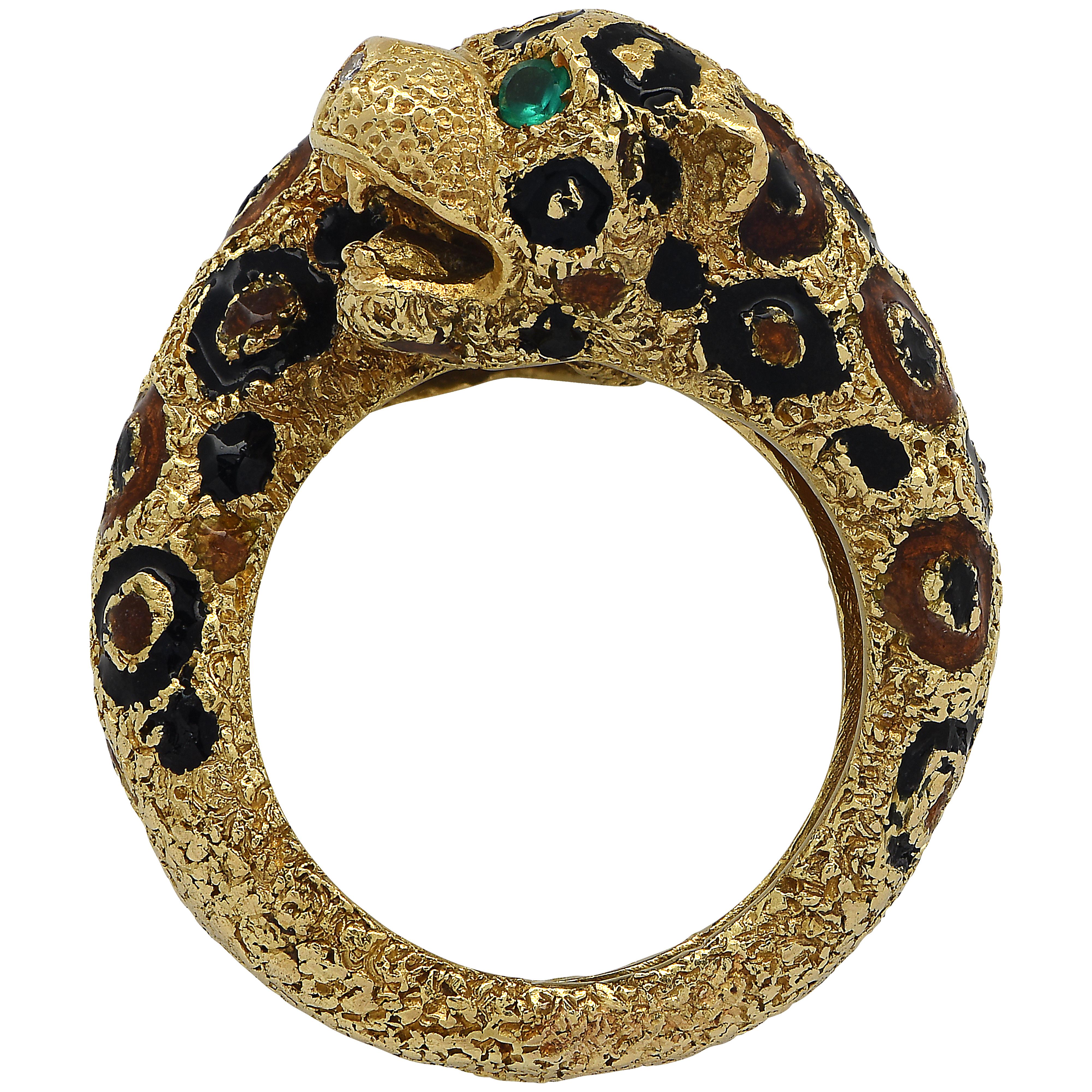Captivating cross over ring crafted in 18 karat yellow gold, featuring two leopard heads accented with green emerald eyes and black and brown enamel spots. This unique ring is a size 6.75 and weight 19.12 grams. It measures 21.5 mm at its widest