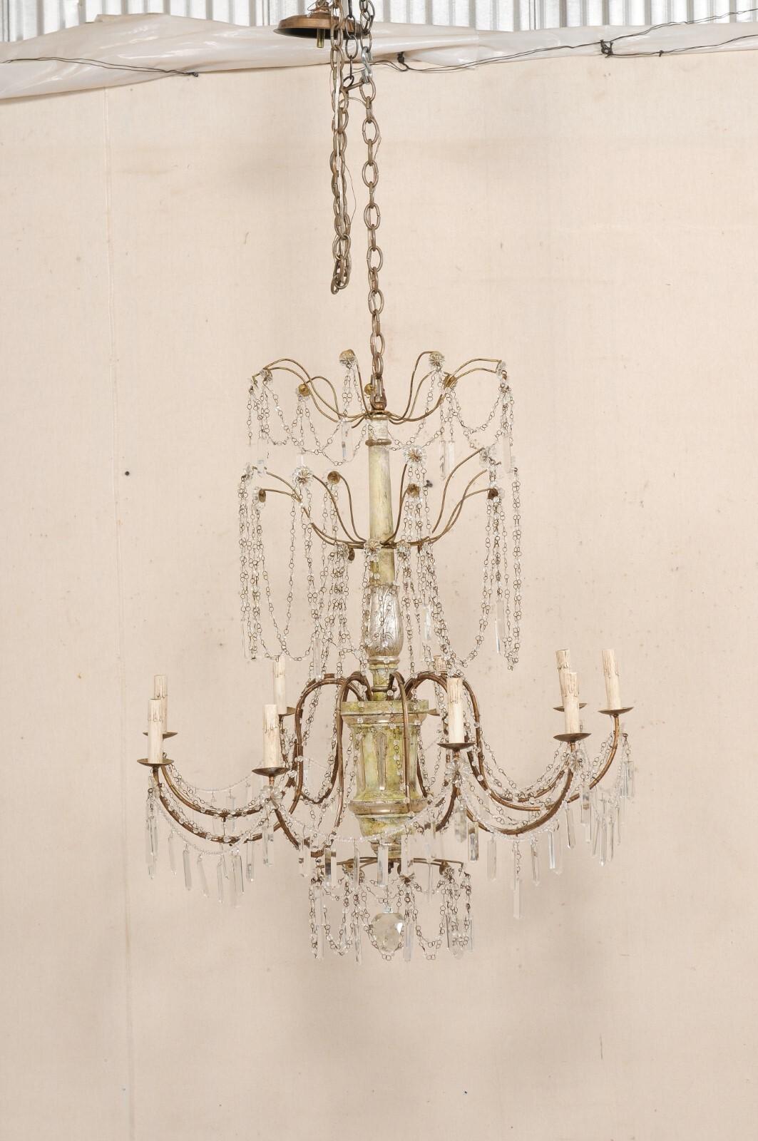 An Italian nine-light crystal chandelier with carved and painted wood central column. This vintage chandelier from Italy has a carved-wood central column, with nine metal s-shaped arms swooping outward, draped with crystal swags and Italian beaded