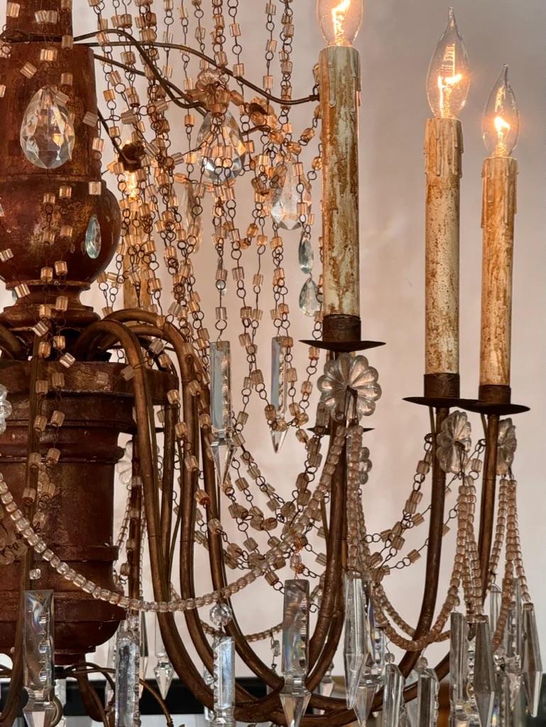 Lustre italien du XIXe siècle à 10 lumières, avec une colonne centrale en bois doré sculpté, deux étages de vastes guirlandes de cristal, avec un mélange de prismes principalement en cristal clair taillés à la main, certains en forme de diamant,