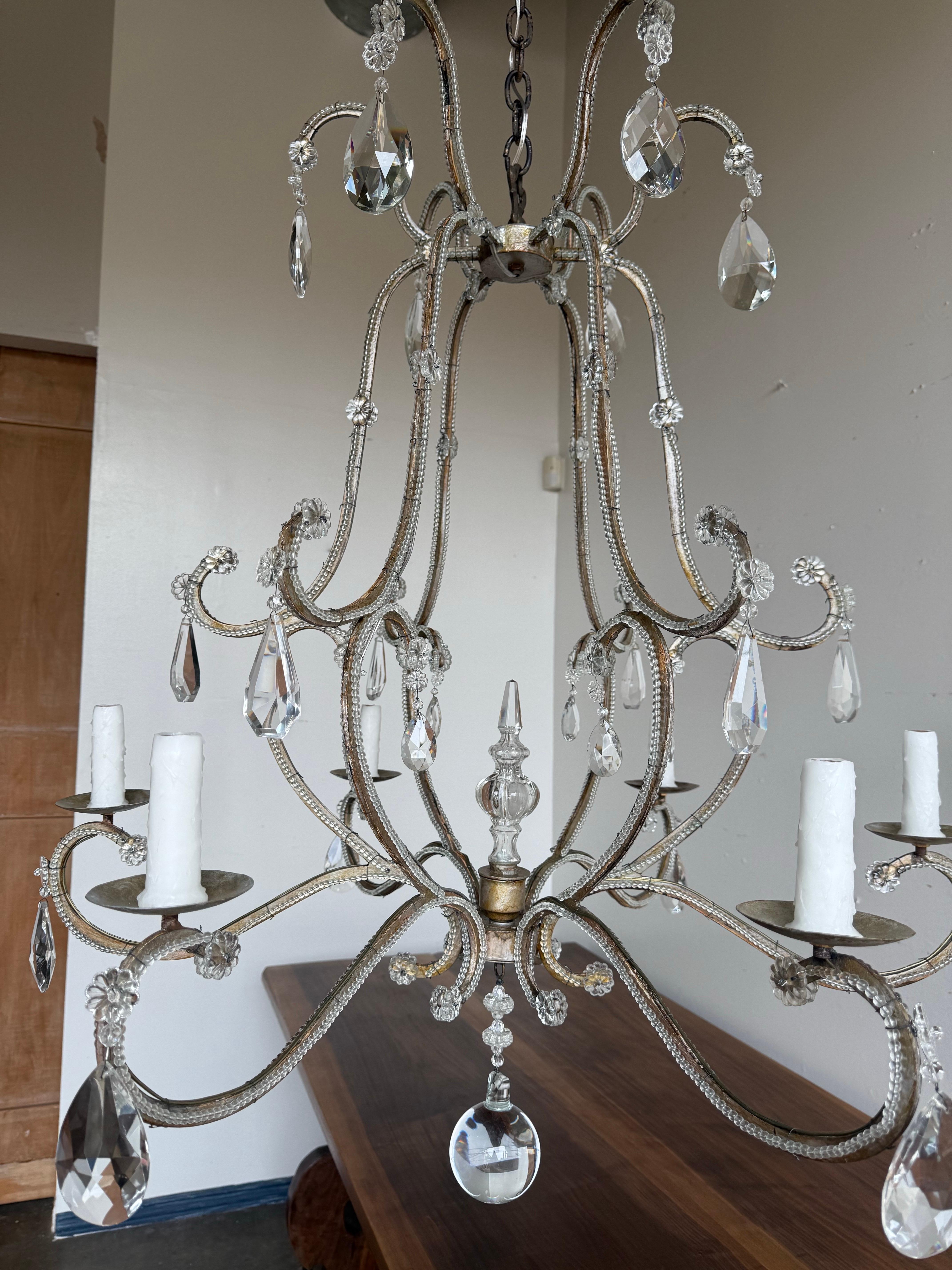 Elegante lampadario italiano in cristallo con perline, metà del XX secolo, con sei luci su bracci graziosamente arcuati e interamente avvolti da perline di cristallo scintillante. L'ariosa cornice in metallo dorato è ornata da prismi e gocce di