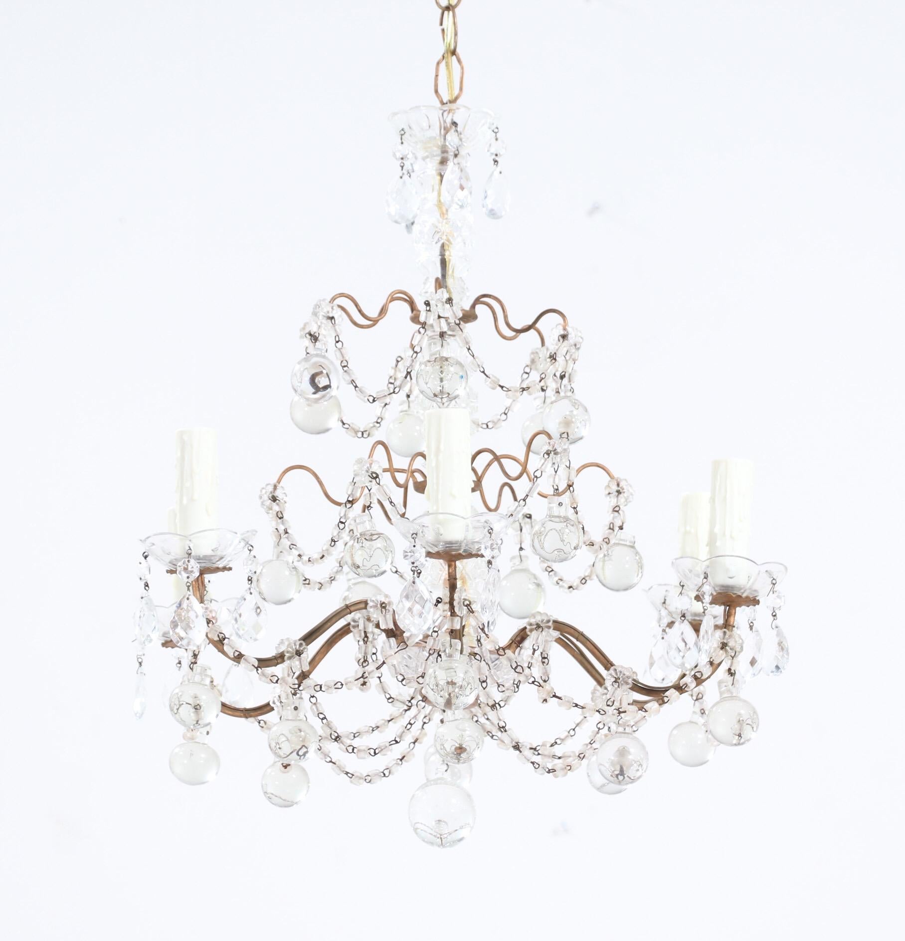 Graceful, 1950s Italian gilt-iron and crystal beaded chandelier.

The chandelier consists of a scrolled gilt-iron frame with a glass column at its center. The chandelier is beautifully decorated with macaroni bead swags and large glass ball