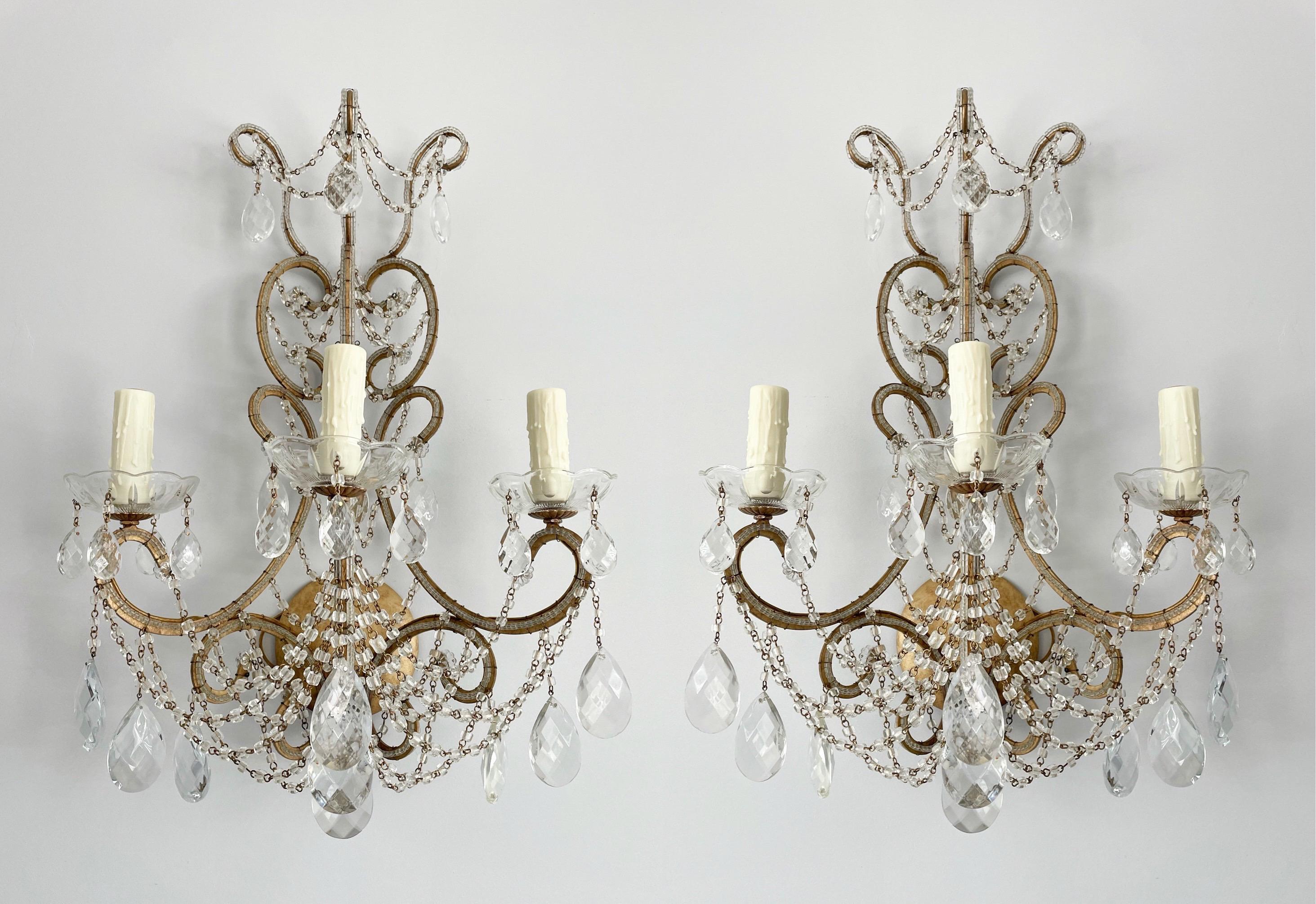 Graceful, vintage Italian pair of gilt-iron and crystal beaded sconces.

Each sconce consists of a scrolled-iron frame outlined with glass beads and decorated with an abundance of macaroni bead swags and faceted prisms. 

The sconces are wired