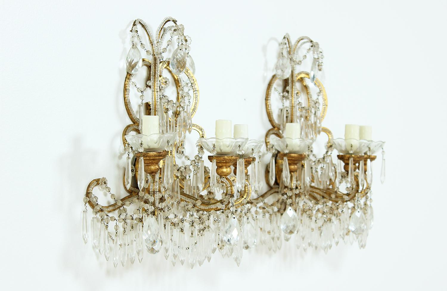 Beautiful pair of 1920s Italian crystal beaded sconces featuring gilt iron frames embellished with crystal beads, swags and prisms. Original wiring is in working condition. Each sconce requires two candelabra base bulbs. New bee wax candle sleeves.