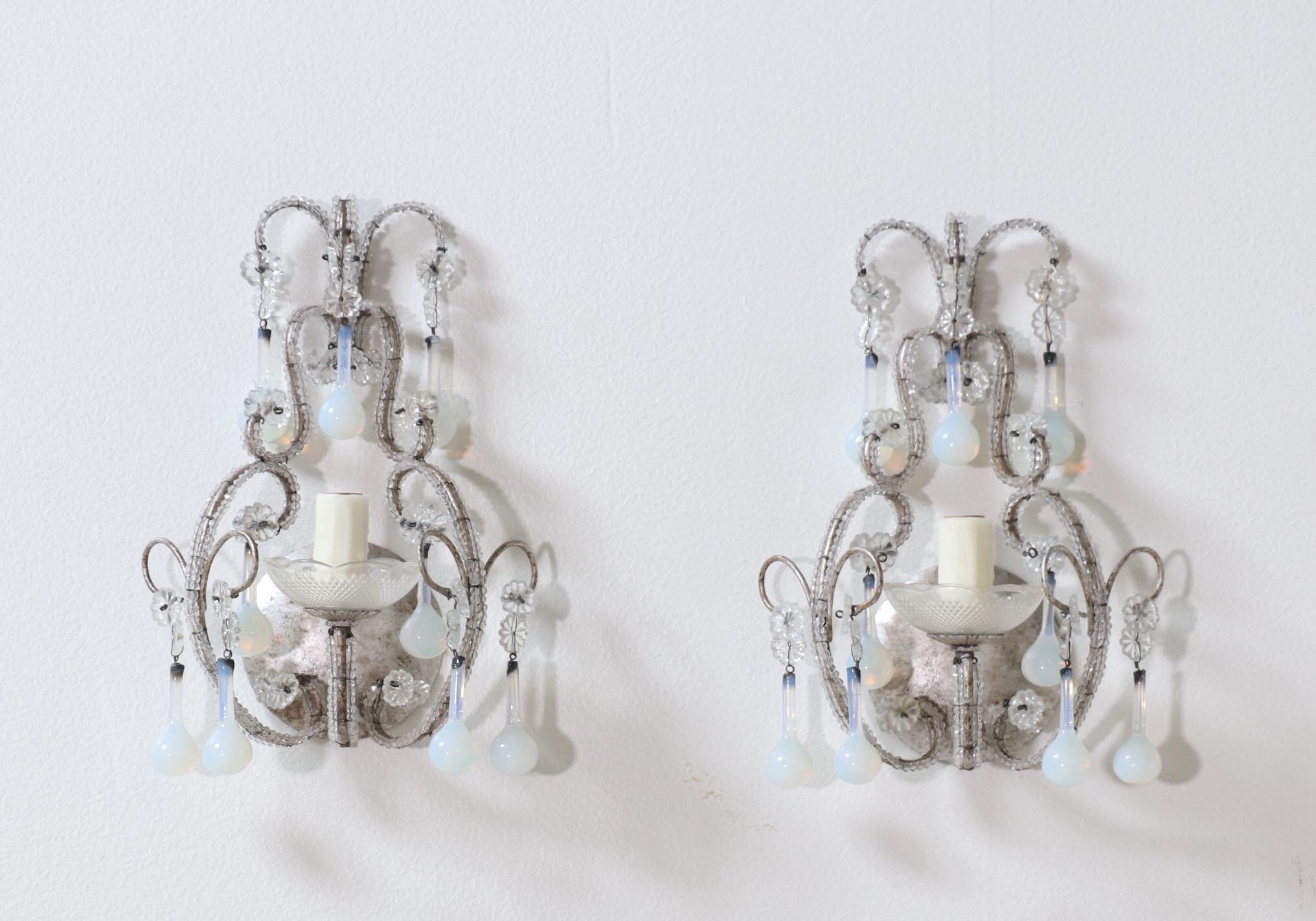 Exquisite, petite-scale crystal beaded sconces with opaline glass drops. 

These small but impactful pair of sconces feature delicate silver-leafed, scrolled-iron frames decorated with rare Murano opaline glass drops.

The sconces require 1