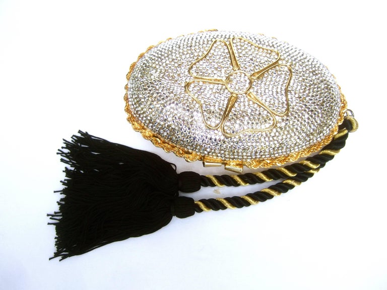 Italian crystal encrusted oval tassel evening clutch c 1980s
The elegant gilt metal minaudière is embellished with rows
of glittering glass crystals on the front exterior 

A sinuous gilt metal flower motif is at the center
Dangling from one side