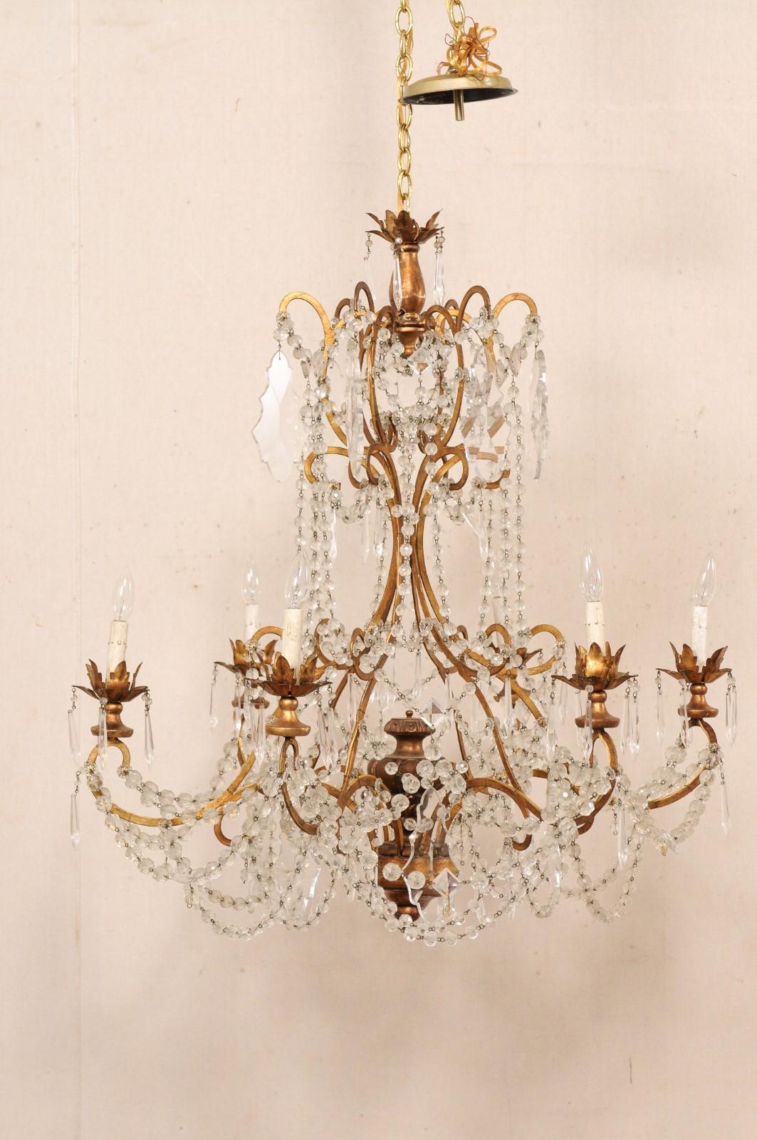 An Italian six-light crystal chandelier from the early to mid 20th century. This antique chandelier from Italy features a scrolling gold-toned armature which is adorn with a crystals and draped in Italian glass bead swags. Six upwardly-scrolling