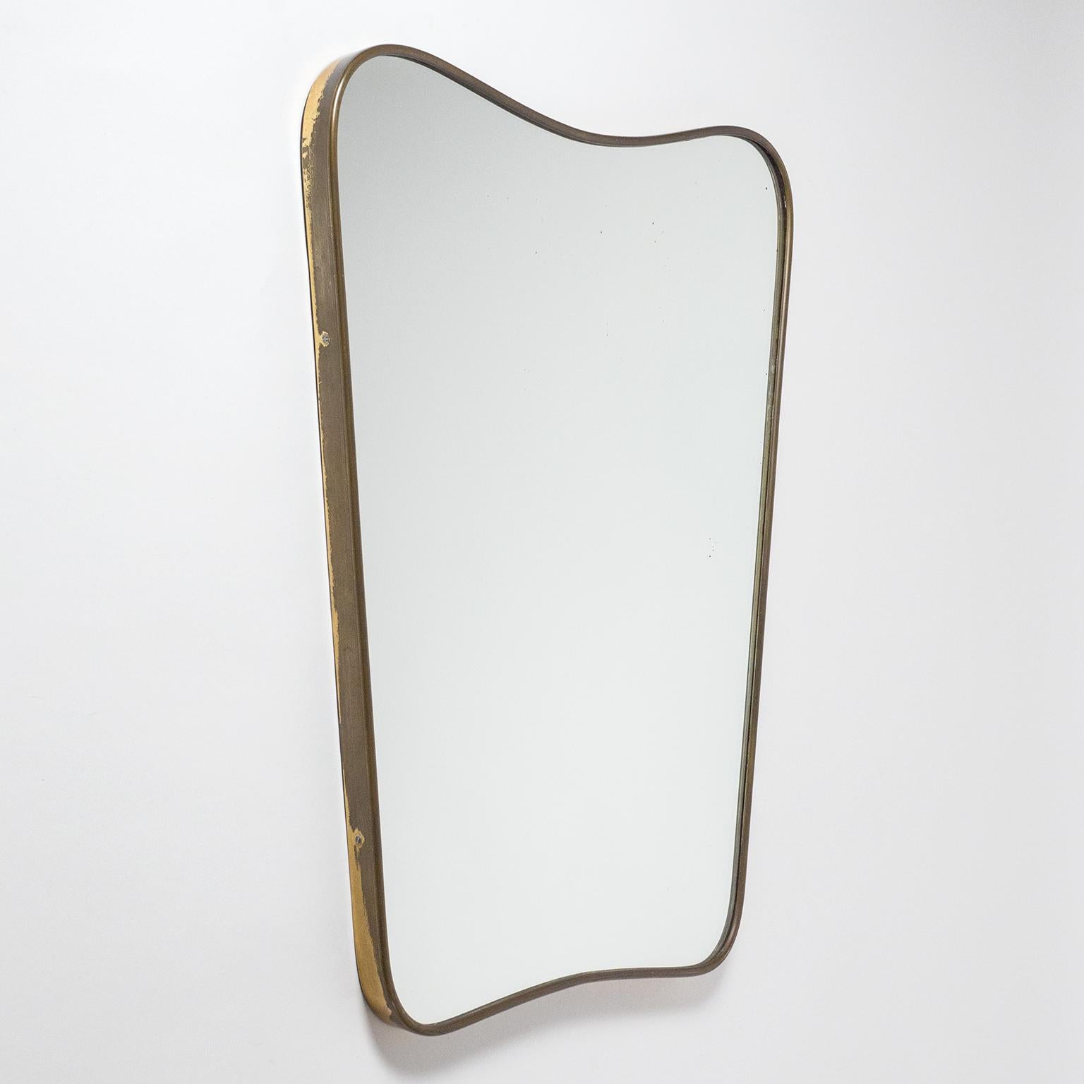 Fine Italian brass mirror in the style of Gio Ponti with a continuous, sensuously sculpted brass rim. Original condition with dark patina on the brass as well as some minor specks on the original mirror. Width on the bottom is 15.5inches/39cm.
