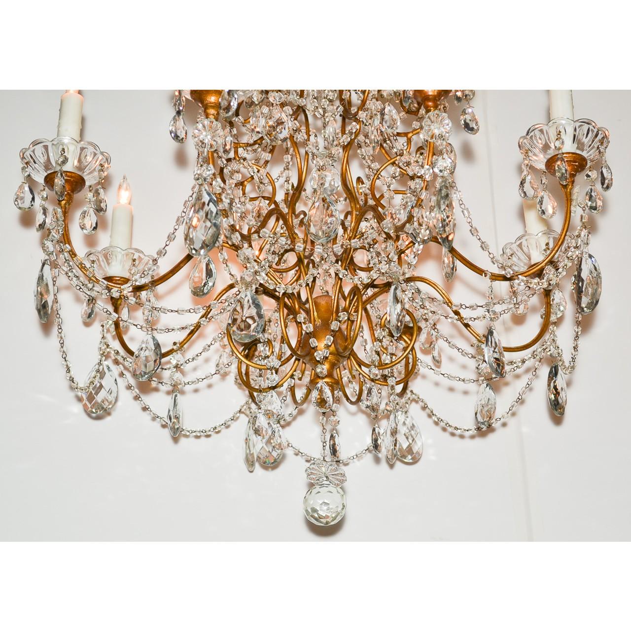 Exquisite Italian crystal and gold gilt tole chandelier with an abundance of scrolled surmounts lavished with faceted almond-shaped prisms, cascading bead crystal drops, and accented with crystal rosettes. Eight wonderfully contoured arms with