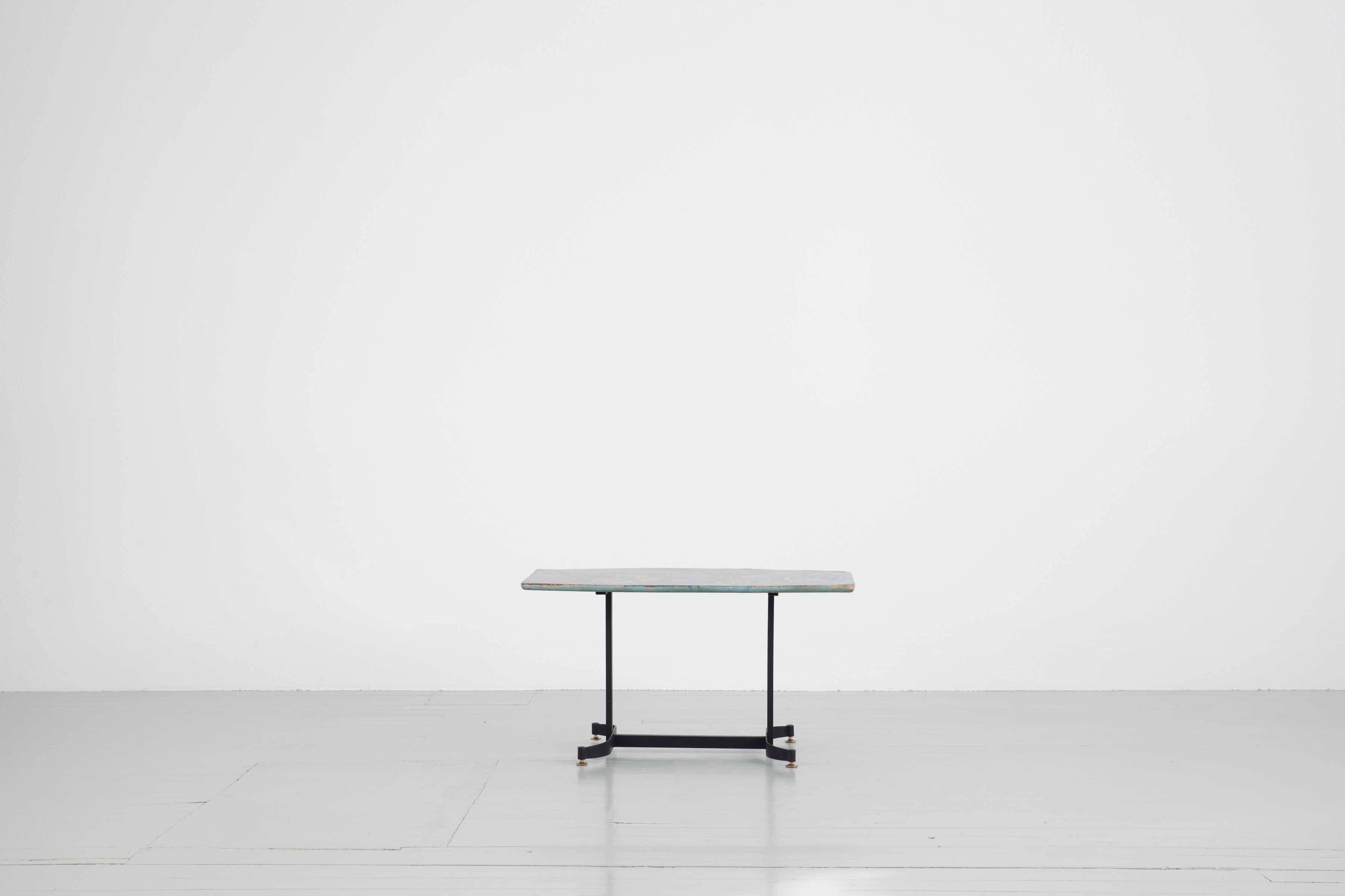 Dieser Sofatisch wurde in den 1950er Jahren entworfen. Das Tischgestell ist aus lackiertem Eisen und Messing, die eckige Tischplatte ist handbemalt. Für das Motiv, das an einigen Stellen (z. B. am Rand) nicht mehr vollständig vorhanden ist, wurden