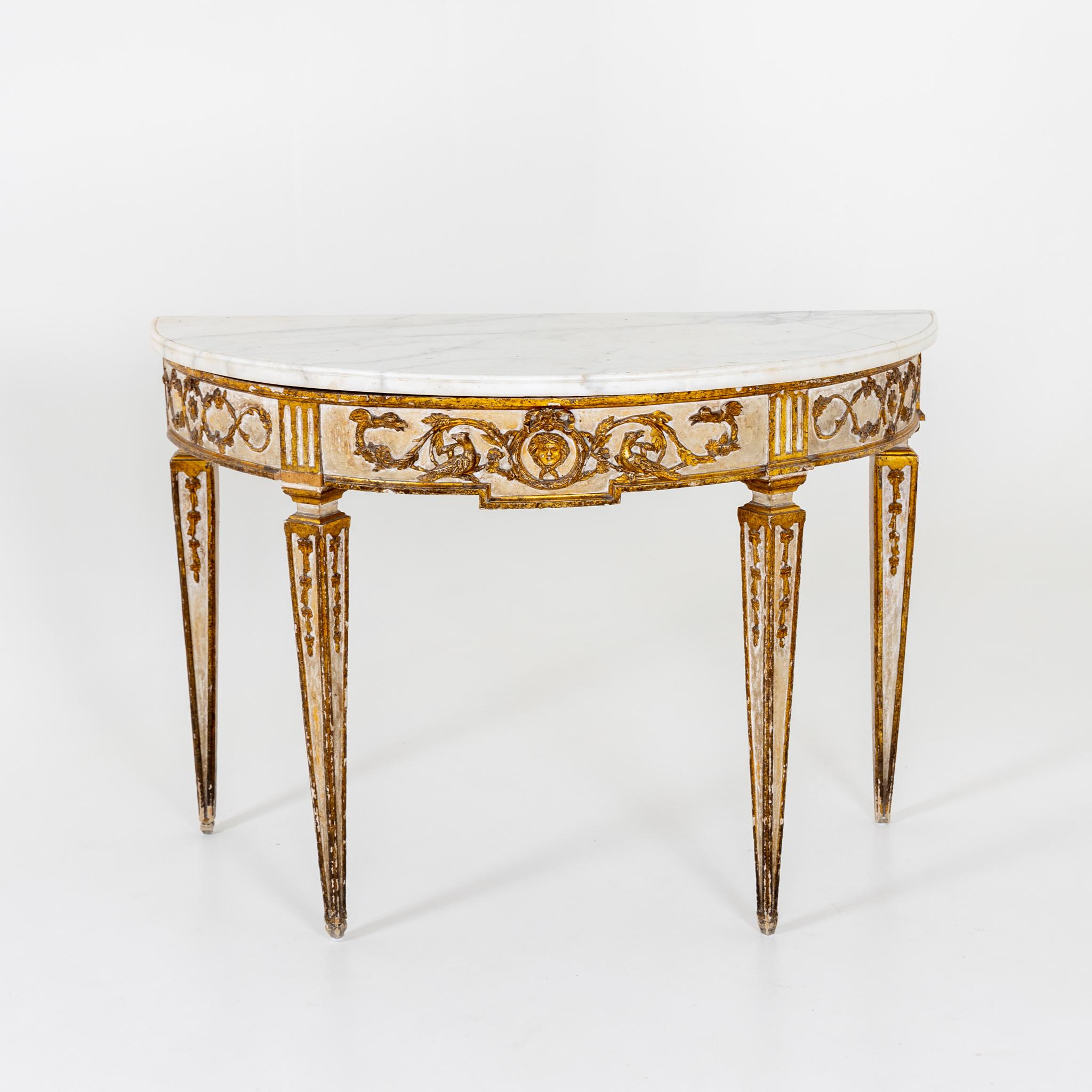 Demi-Lune console standing on tall square-pointed feet with gold-patinated decoration in the form of vines and mascarons in relief and a white marble top.
