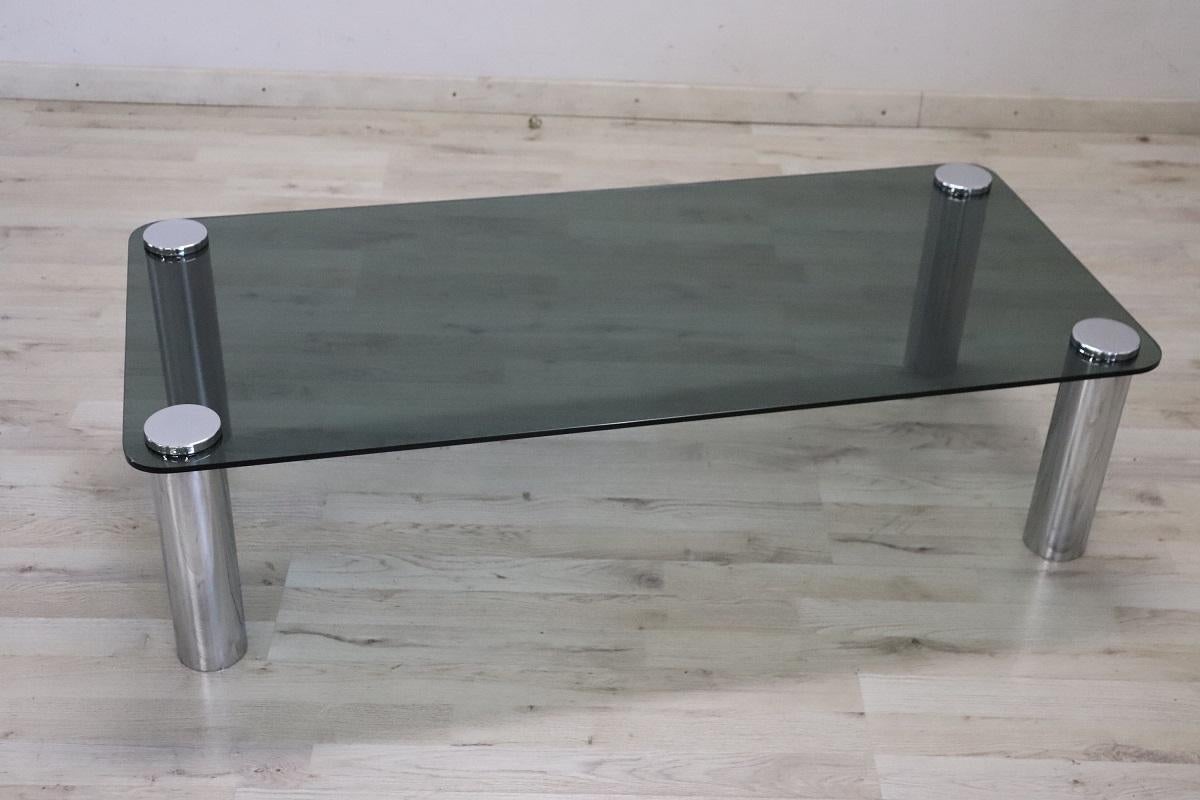 This is a beautiful and sophisticated piece of 20th-century furniture. 1970s Italian design is distinctive and evident in this rectangular coffee table.

Made with minimalist cylindrical chromed metal legs and a smoked glass top. Its lines and