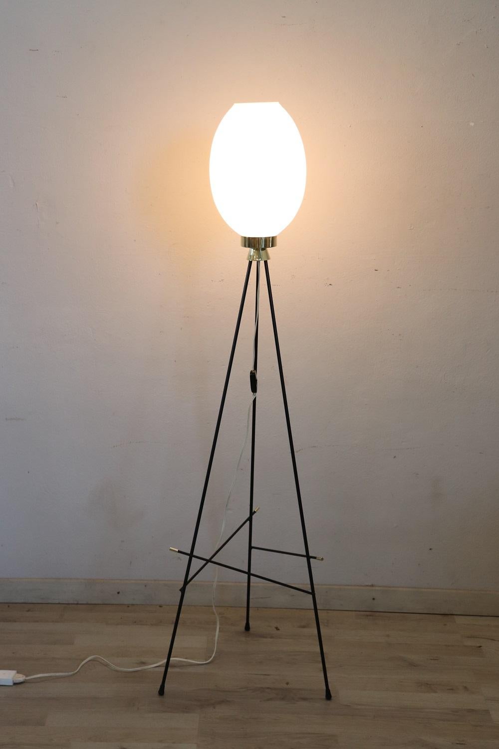 Beautiful Italian design stilnovo style floor lamp, 1950s. A tyrpod lamp characterized by a white opaline glass lampshade, black painted metal structure and golden brass details. Beautiful for a modern and vintage environment. Perfect conditions