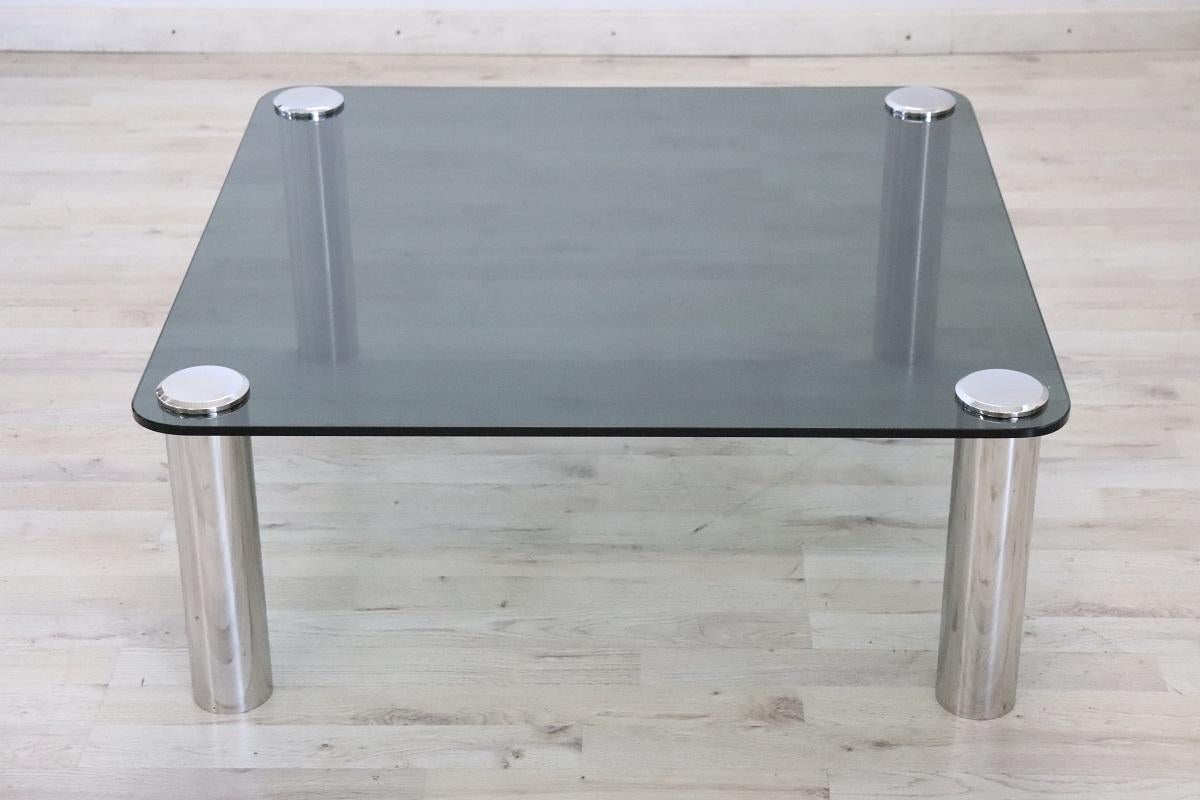 Si tratta di un bellissimo e sofisticato mobile del XX secolo. Il design italiano degli anni '70 è evidente in questo tavolino quadrato.

Realizzato con gambe minimal in metallo cromato di forma cilindrica e piano in vetro fumé. Questa linea di
