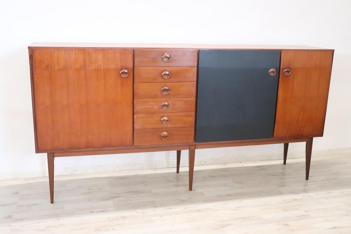 Beautiful 1960s Italian design long sideboard in teak veneer. Characterized by a very linear minimalist style with the particular use of two colours, wood color and a black lacquered door. Equipped with ample useful space with three doors and