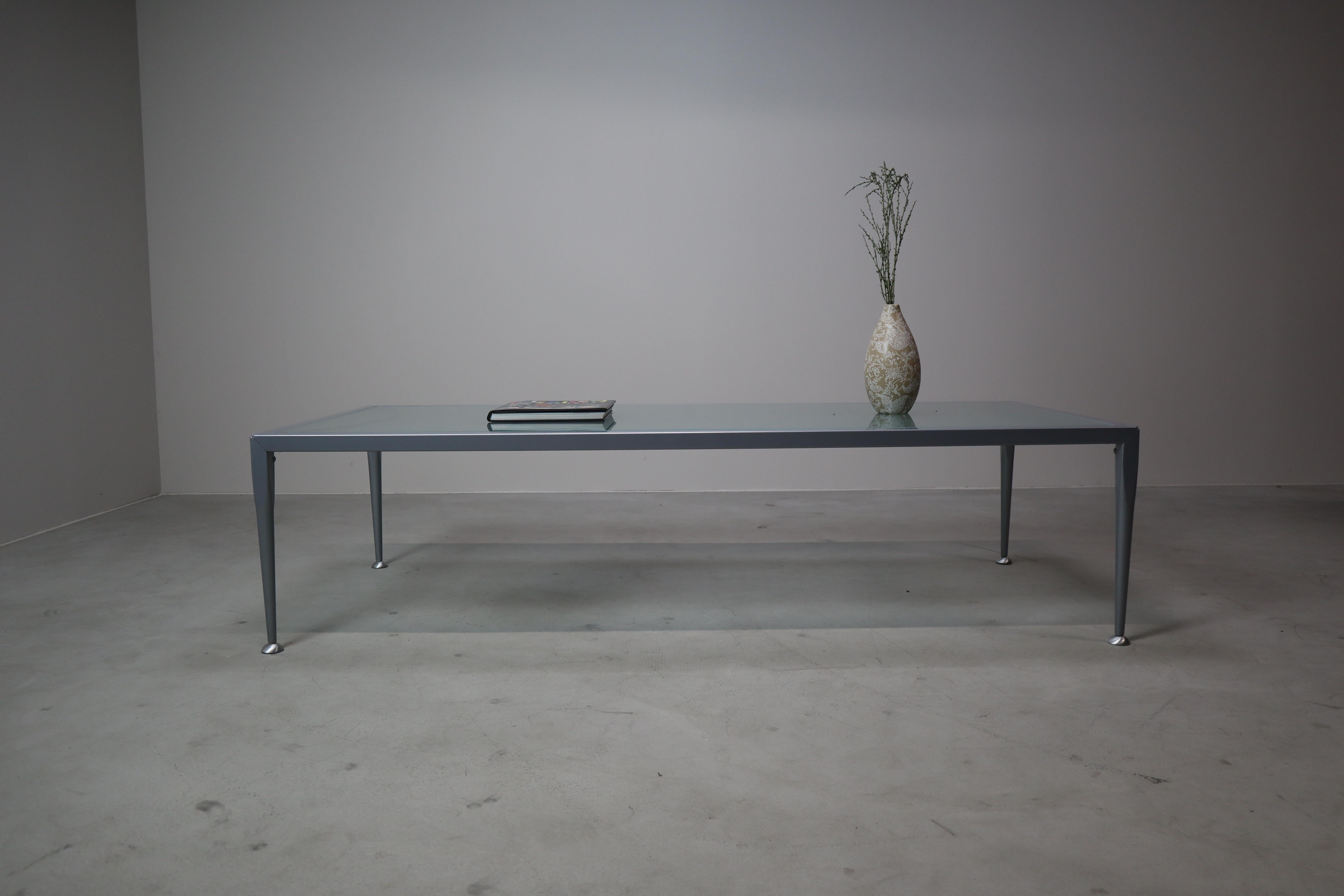 This minimalist coffee table by Baleri Italia is a beautiful example of refined Italian design from the 1990s. The sleek, architectural frame is made from lacquered metal in a cool grey tone, supporting a frosted glass top with subtle curved lines