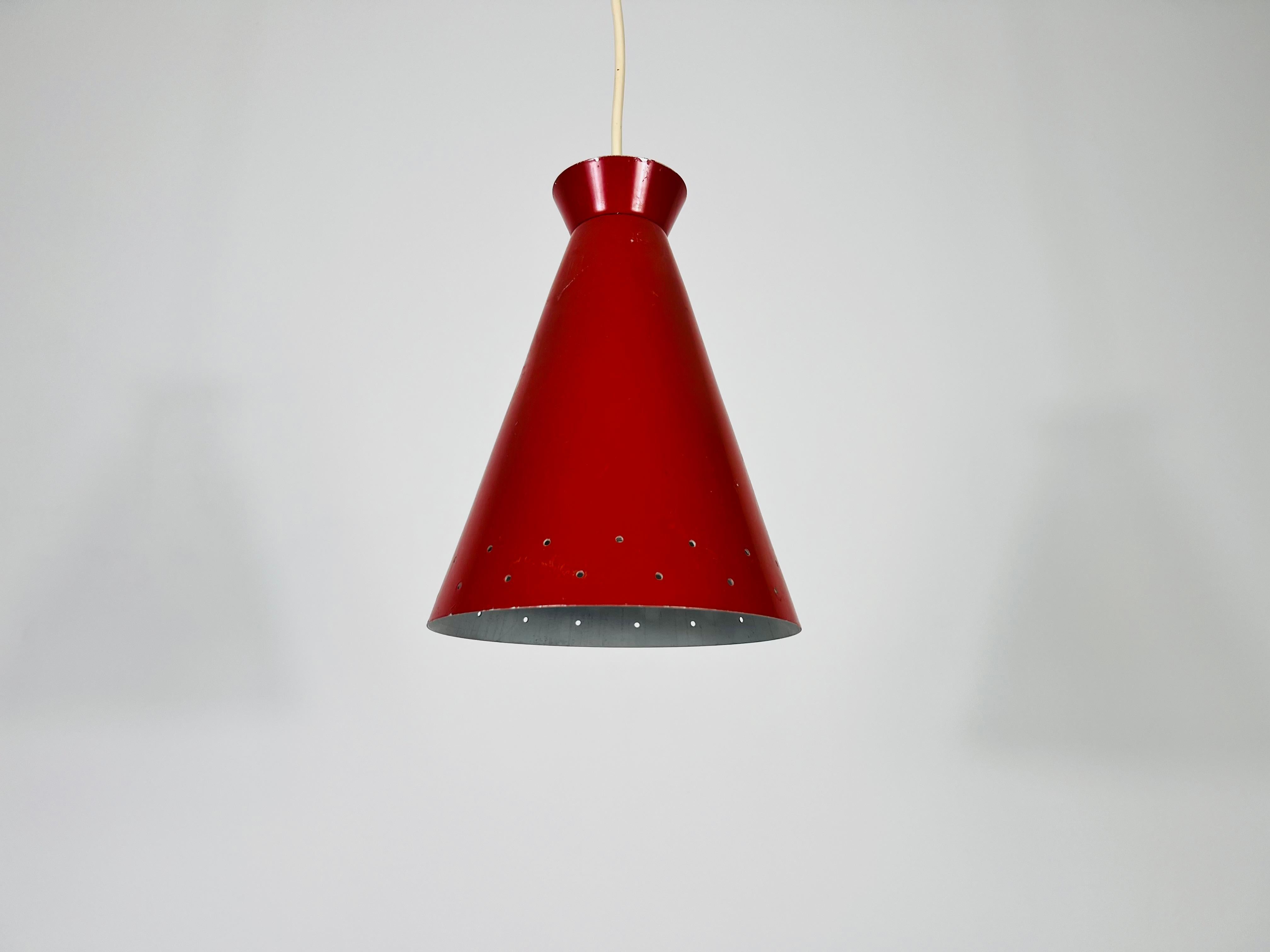 This stunning Italian hanging lamp from the 1950s features a distinctive Diabolo shape, showcasing a beautiful red color and perforated metal design. With its conical form, this piece epitomizes mid-century modern design. This elegant lamp is a