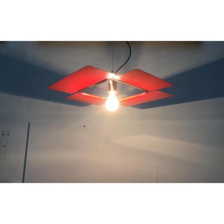 Very rare pendulum from Guzzini based on a design by Fabio Lenci from the 70s.
The lamp has a particularly flat design. This design actually consists entirely of a large barndoor, like those seen in film lights. This gives the lamp a very technical