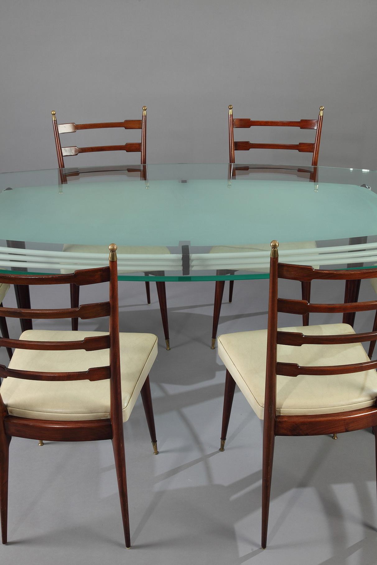 White lacquered metal table with glass top resting on four slender oak feet. 1960s Italian design. Six chairs in mahogany and leather imitation decorated with brass finials, 

circa 1960
Dimensions table: L 188 cm, P 116 cm, H 78 cm.
Dimensions