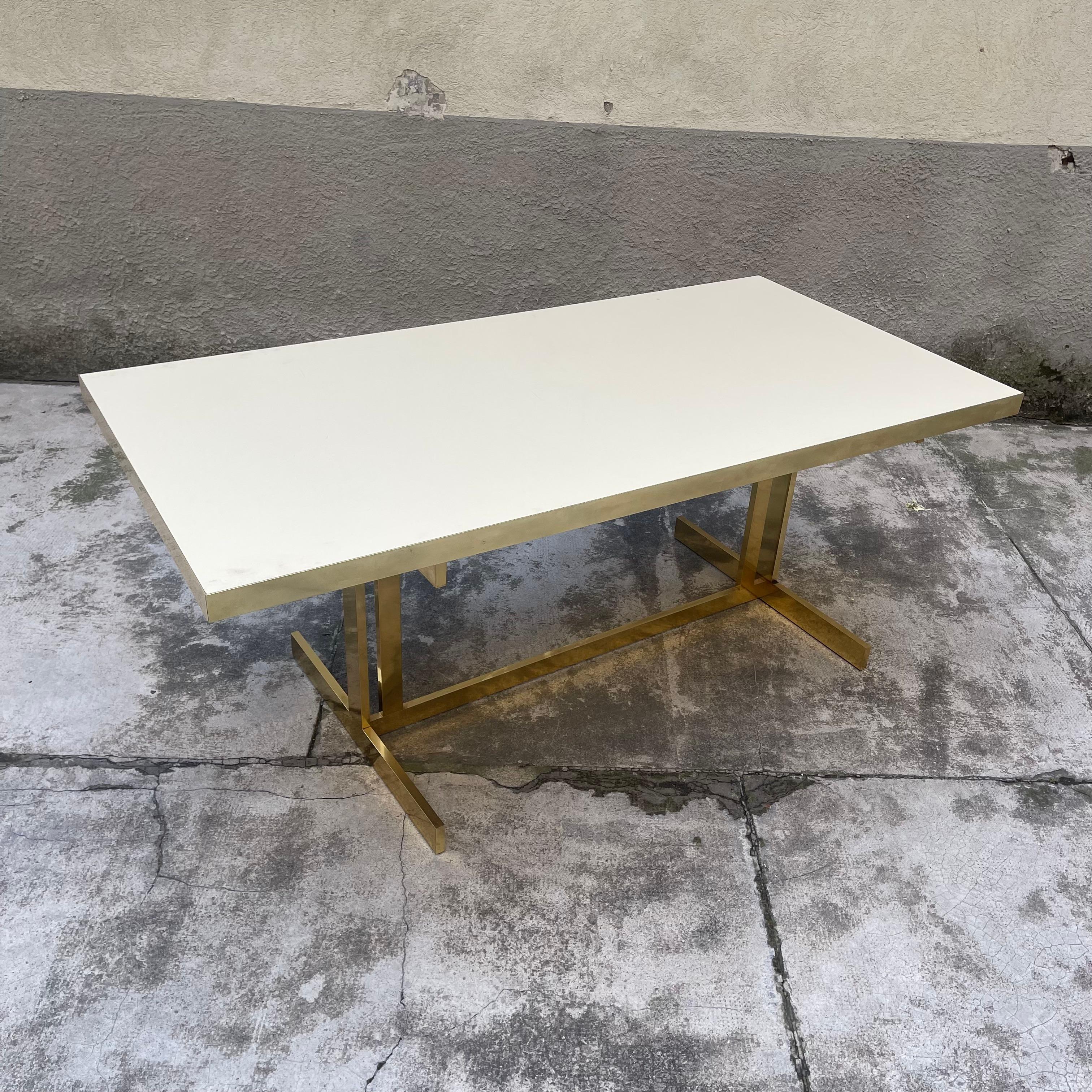 This marvel of a table consists of a rectangular-section brass tubular frame supporting a massive ivory-colored laminate top edged with brass bands. It can be accompanied by 4 chairs of the same manufacture, as visible from the photos. The latter