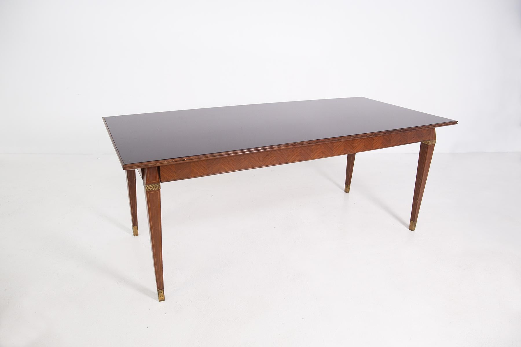 Italian dining table in the style of Paolo Buffa from the 1950s.
The table has wood grain and small painted elements in its legs.
The table legs have a prism shape and as a final element there is a brass ferrule. In the upper part of the leg there