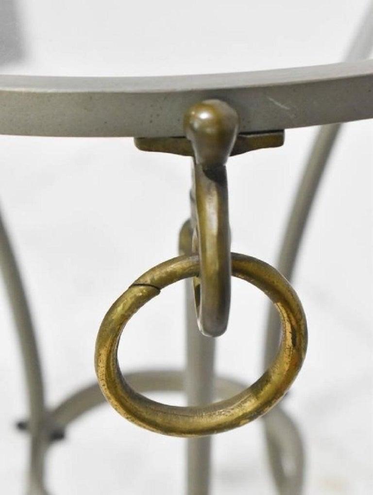 An Italian Directoire style vintage steel pair of side tables or gueridons from the mid 20th century, with brass rams' heads and hoofed feet. Created in Italy during the midcentury period, this side table features a circular glass top supported by