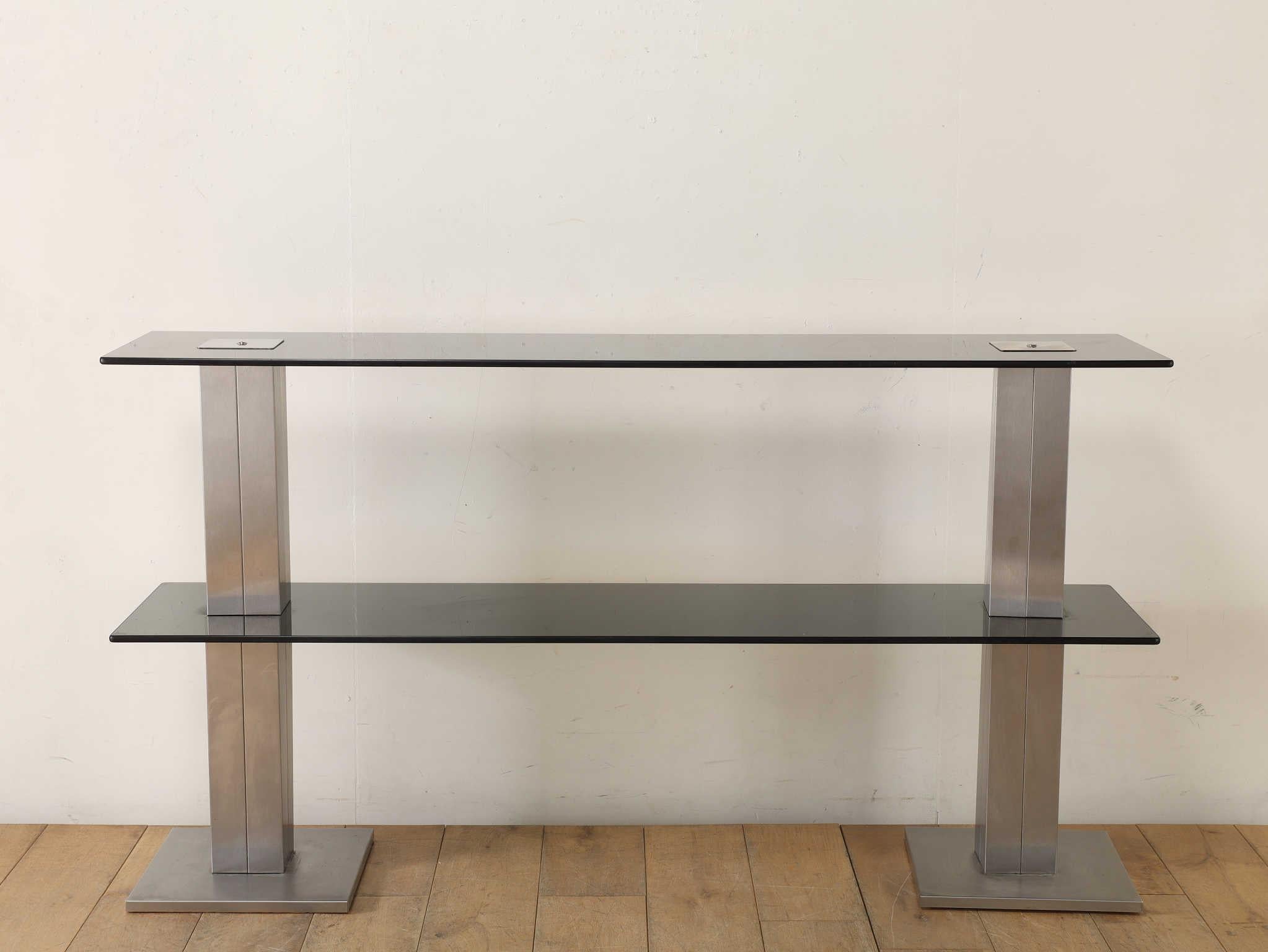 This display shelf features a striking composition of clean, linear forms, showcasing the refined interplay between chrome and glass. The sleek metallic framework provides a contemporary edge, while the transparent glass surfaces add lightness and