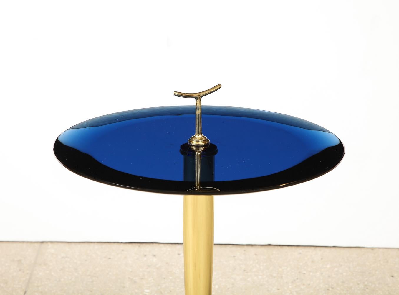 Polished brass, colored glass. Brass frame with 3-pronged foot and stylized finial/handle. Thick, circular blue glass table surface with elegant beveled edge.