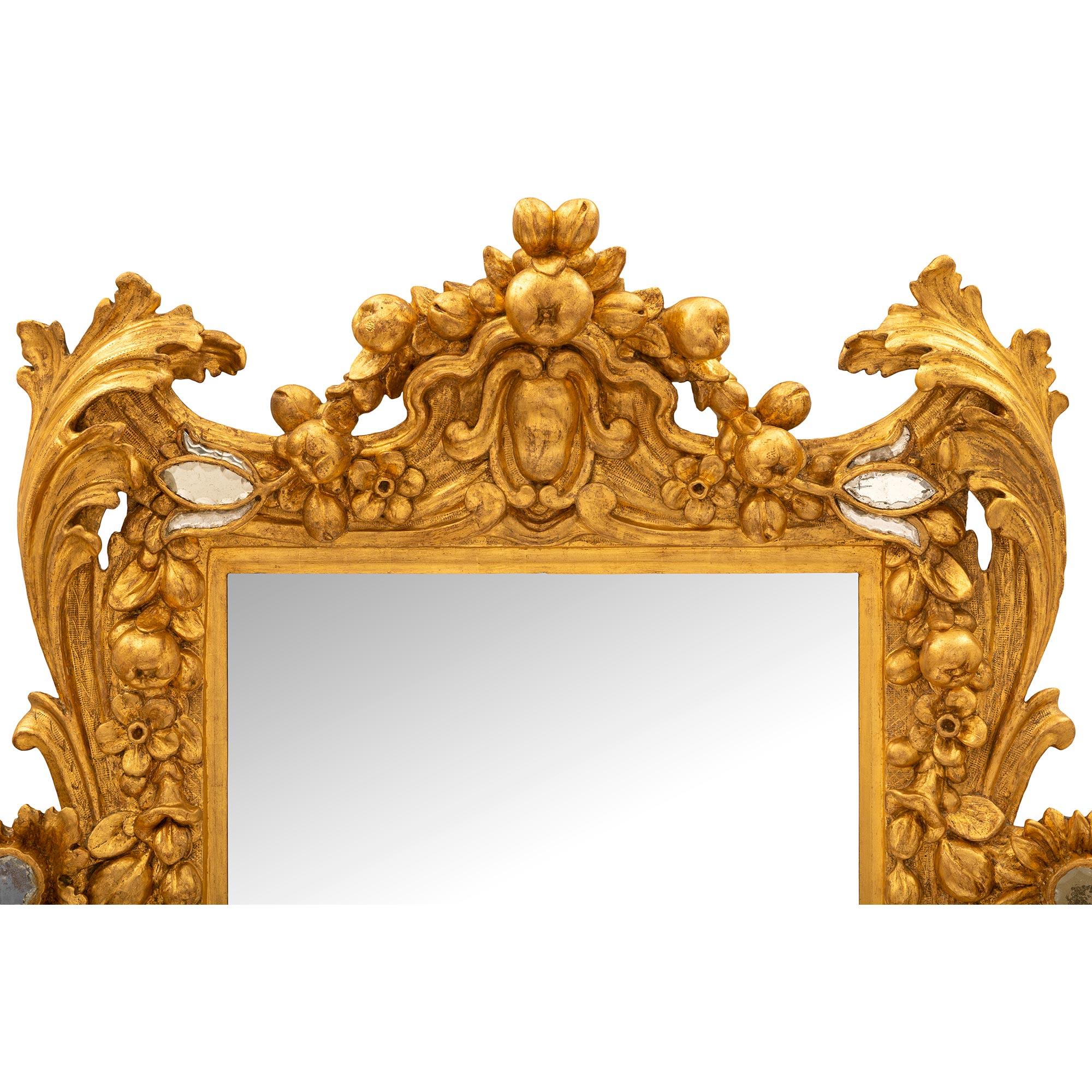 A stunning Italian early 18th century Baroque period giltwood and cut glass mirror. The central rectangular mirror plate is set within a fine mottled border with exceptional finely detailed carvings extending throughout the frame. At the base is a