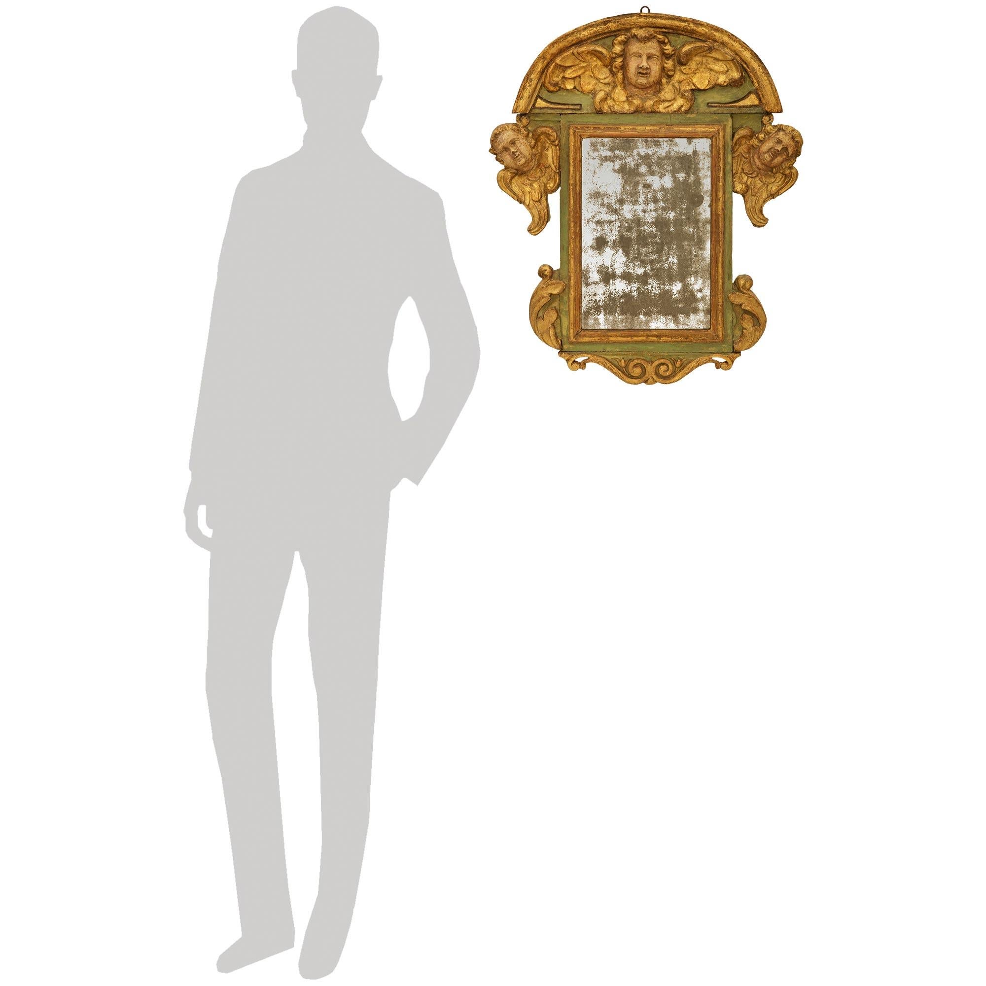 An elegant and most charming Italian early 18th century Baroque Period patinated Wood and Giltwood mirror. This wonderful mirror displays its original patinated mirror plate set within a mottled Giltwood border. At the base is a scrolled Giltwood