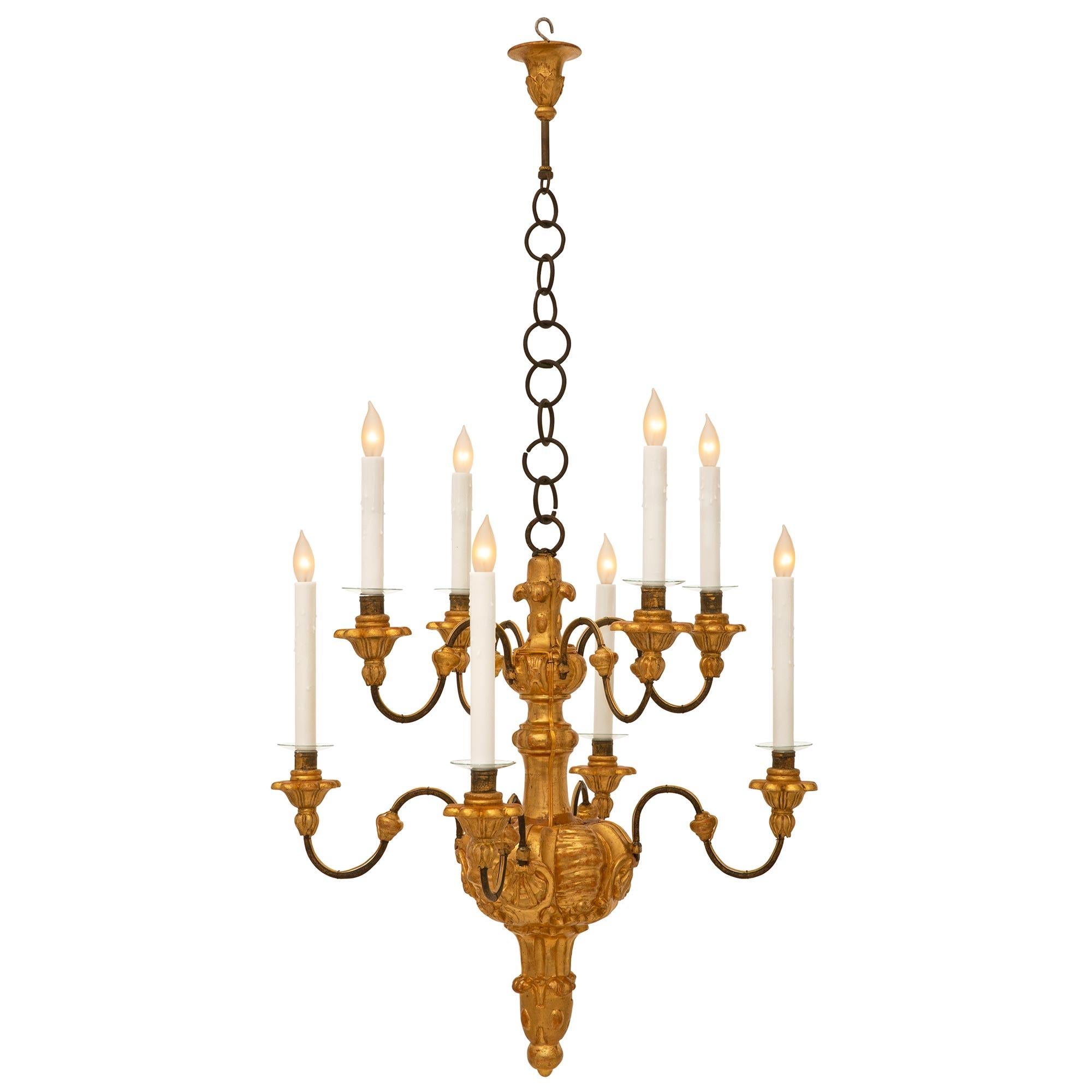 A beautiful and most decorative Italian early 18th century giltwood and wrought iron chandelier. The eight arm chandelier is centered by a beautiful bottom foliate finial with lovely fluted designs below a reeded reserve with striking seashells from