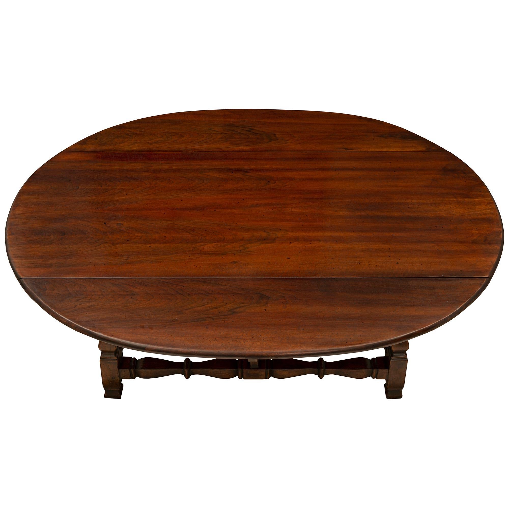 A beautiful Italian early 18th century Tuscan st. Walnut gateleg dining table. The table is raised by elegant mottled feet below striking richly carved squared and baluster shaped legs each connected by a stretcher with similar designs. Above is the