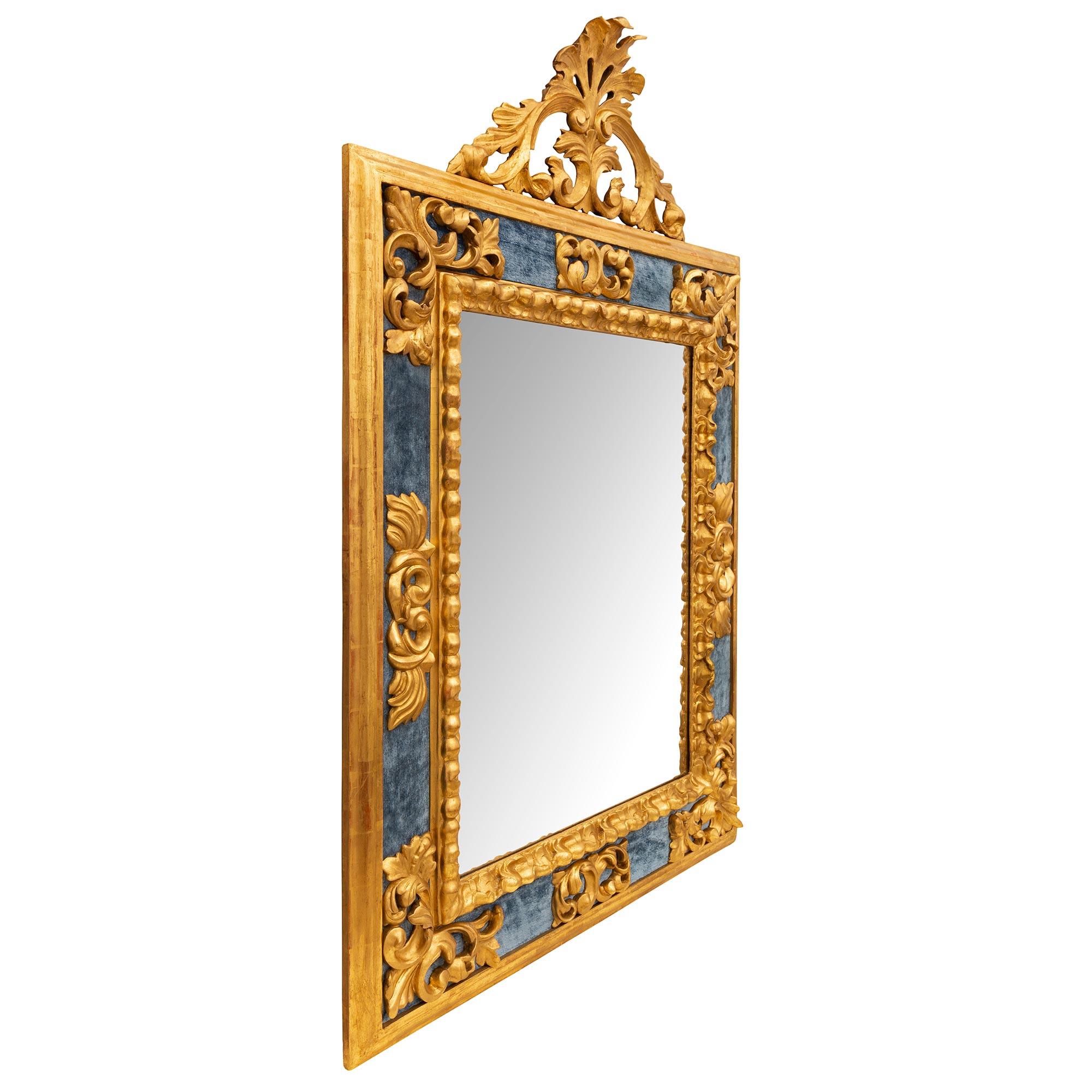 A unique and most decorative Italian early 19th century Baroque st. giltwood and blue velvet mirror. The original mirror plate is framed within a beautiful mottled carved foliate band leading out to lovely richly carved scrolled pierced foliate