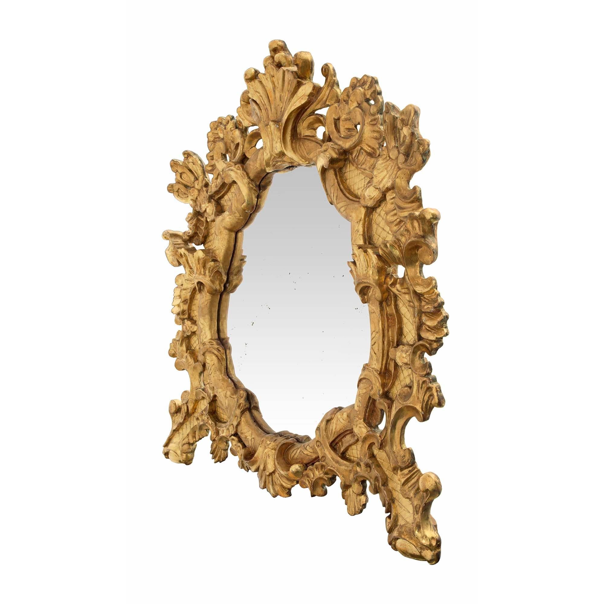 Un beau et unique miroir baroque italien du début du 19ème siècle en bois doré. Le miroir est surélevé par deux pieds très décoratifs avec de grandes feuilles d'acanthe enroulées et un fin motif de treillis qui s'étend sur tout le cadre. La plaque