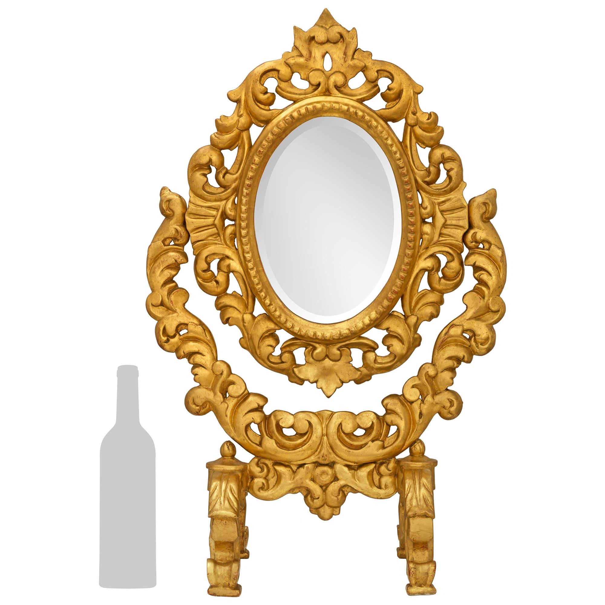 Un élégant et très décoratif miroir baroque italien du début du 19ème siècle en bois doré. Ce magnifique miroir de courtoisie à poser est surélevé par deux supports à double volute décorés de feuilles d'acanthe et de charmants épis de faîtage. Les