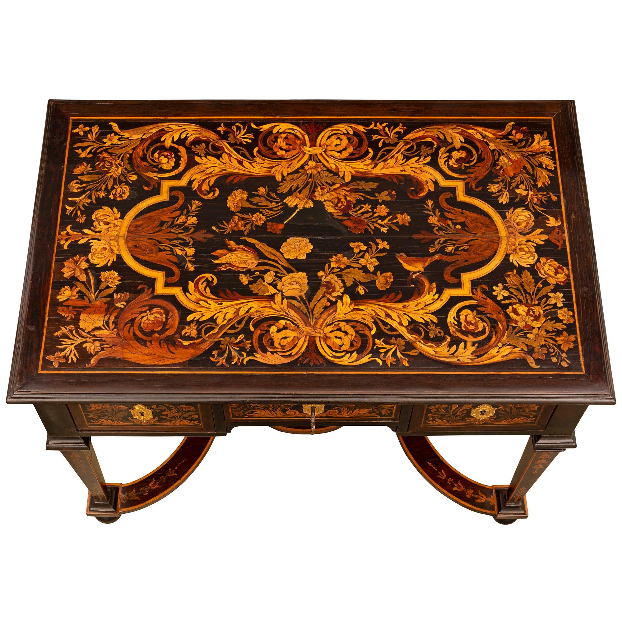 An exceptional Italian early 19th century ebonized fruitwood, exotic wood, and ormolu desk. The three drawer desk is raised by elegant square tapered legs with bun feet and finely inlaid foliate designs. Each leg is connected by a charming stretcher