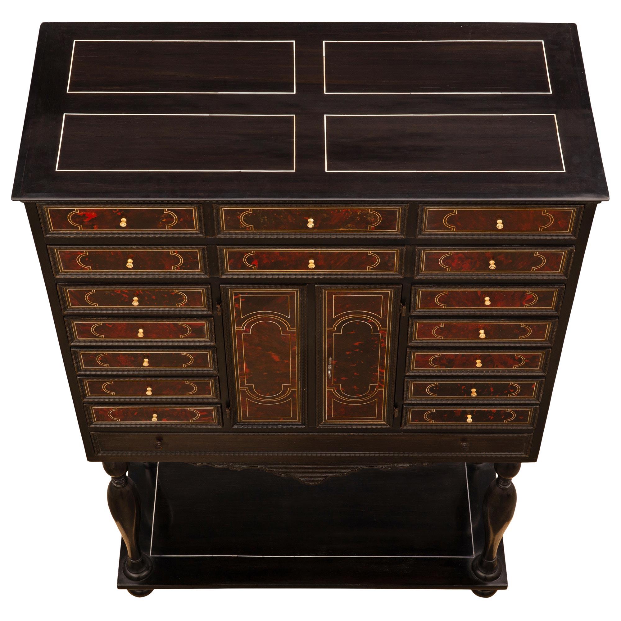 Espectacular vitrina italiana de principios del siglo XIX de ébano, carey y hueso. El mueble de dos puertas y veintidós cajones se eleva sobre elegantes patas de bollo bajo un nivel inferior rectangular decorado con un filete de hueso finamente