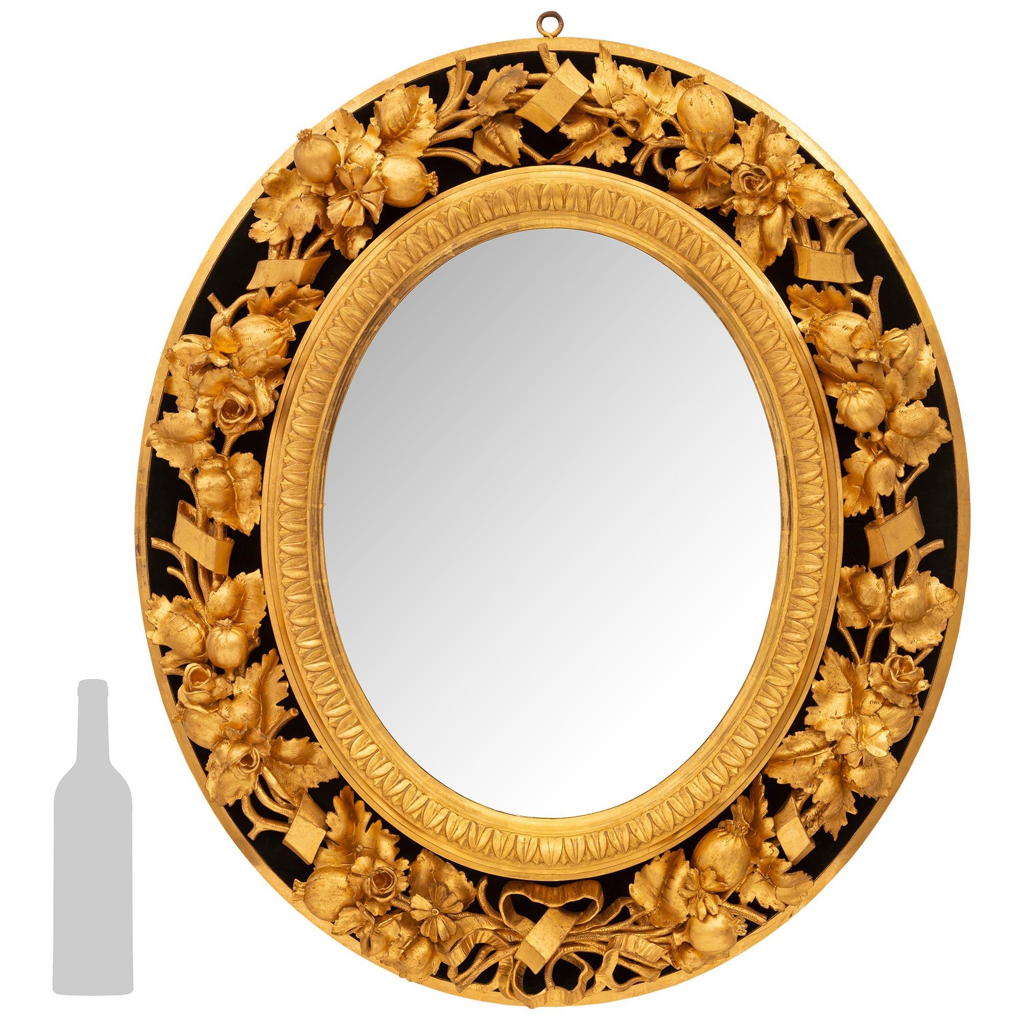 A sensational Italian early 19th century Giltwood and black Velvet mirror. This most unique mirror is set within an oval frame decorated by a richly carved floral band of blossoming flowers, oak leaves and pomegranates set on a black velvet