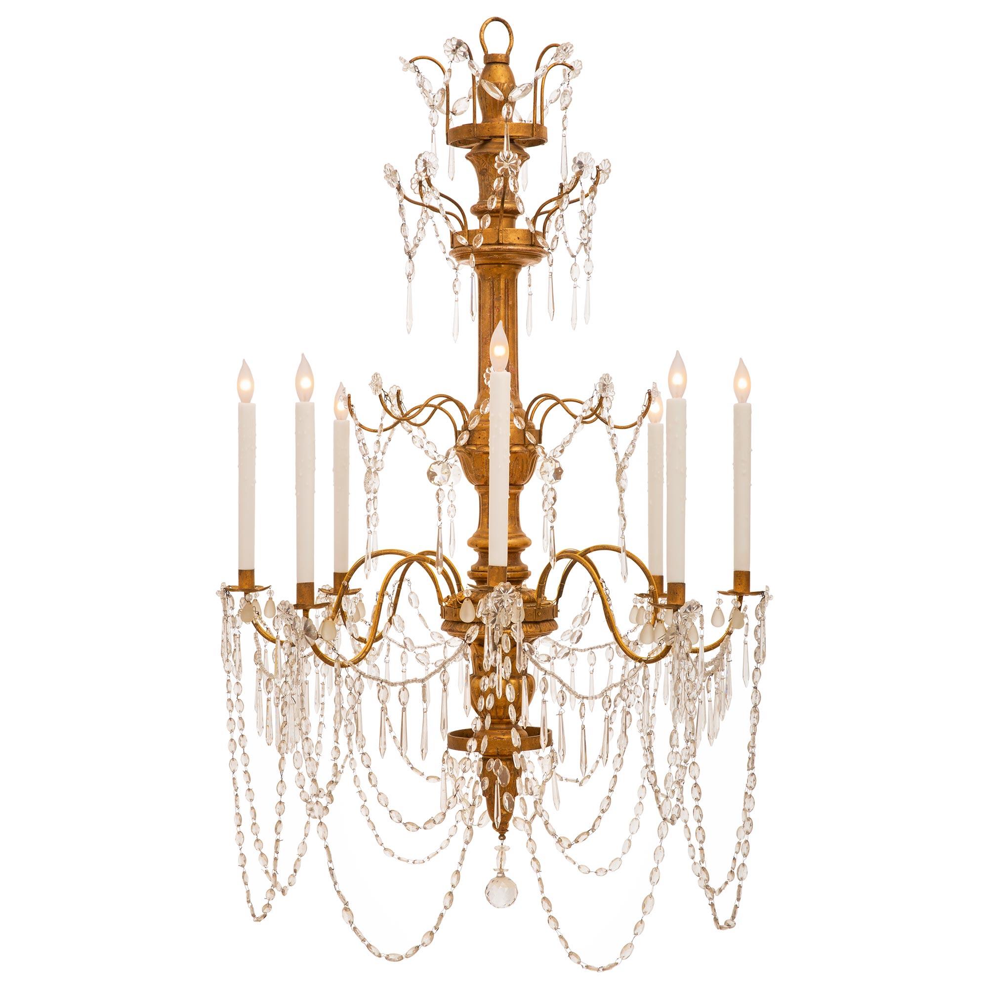 An early 19th century Italian giltwood, glass and crystal eight light chandeliers. This elegant chandelier has a carved giltwood central fut with bottom finial and crystal ball pendant. Crystal garlands join the 'S' scrolled metal arms. Additional