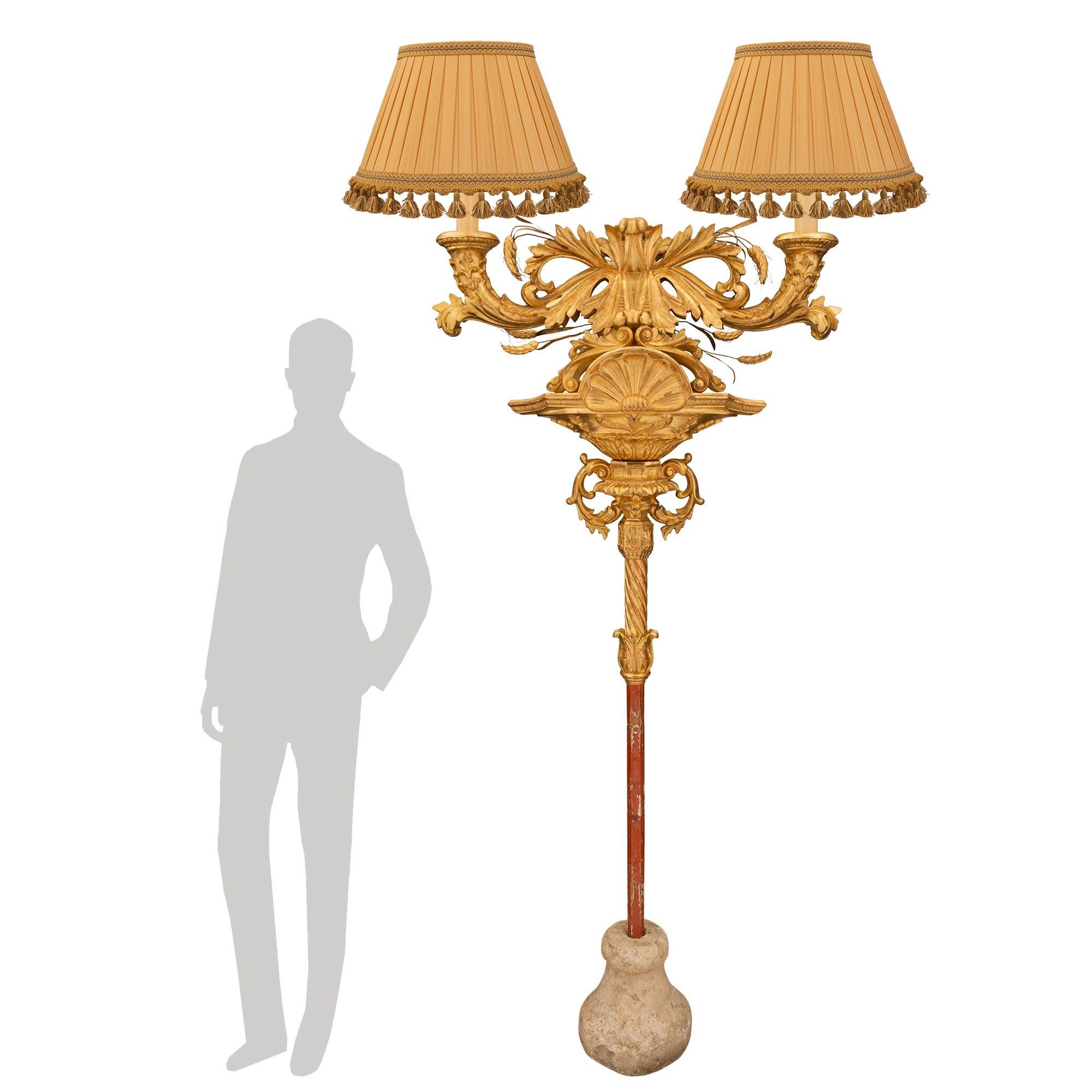 Un monumental lampadaire italien en bois doré du début du XIXe siècle. La lampe est soutenue par la base originale en pierre sous le fut patiné couleur sang de boeuf. Le fut se poursuit avec une feuille d'acanthe en bois doré et un motif torsadé