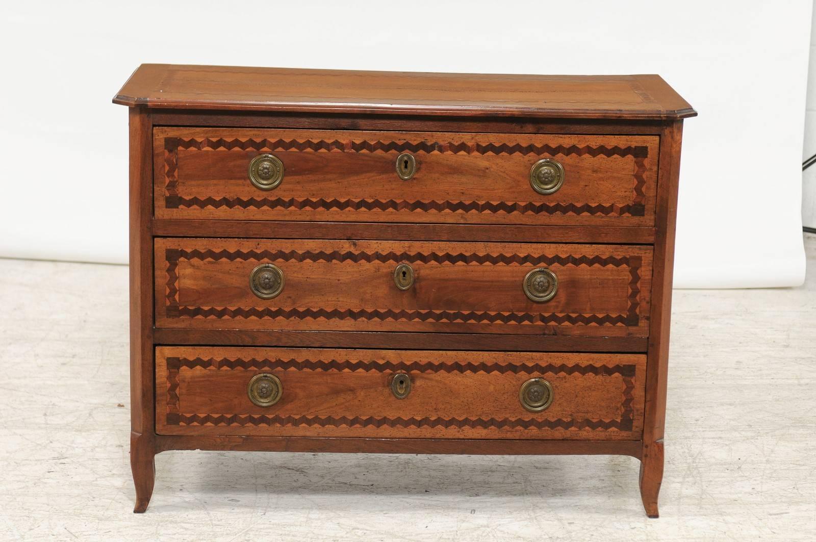 An Italian three-drawer marquetry commode with inlaid zigzag patterns from the early 19th century. This Italian commode features a rectangular top with canted corners in the front, delicately inlaid with zigzag motifs. The façade, made of three