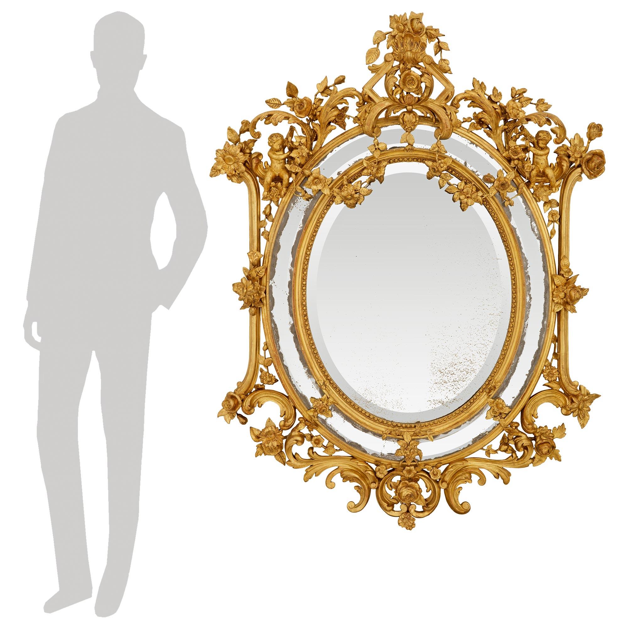 Un sensationnel et très décoratif miroir italien en bois doré de style Louis XV du début du 19ème siècle. Ce miroir en bois doré à double encadrement est centré en bas par une charmante réserve de rose simple flanquée de rinceaux et menant à