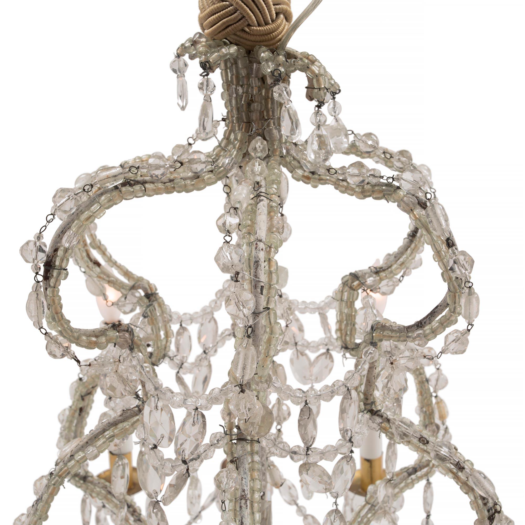 A beautiful Italian early 19th century Louis XV st. patinated off white iron and gilt metal twelve arm chandelier. The patinated off white iron cage has a wonderful open scrolled design. The frame is elegantly decorated by small beaded strands