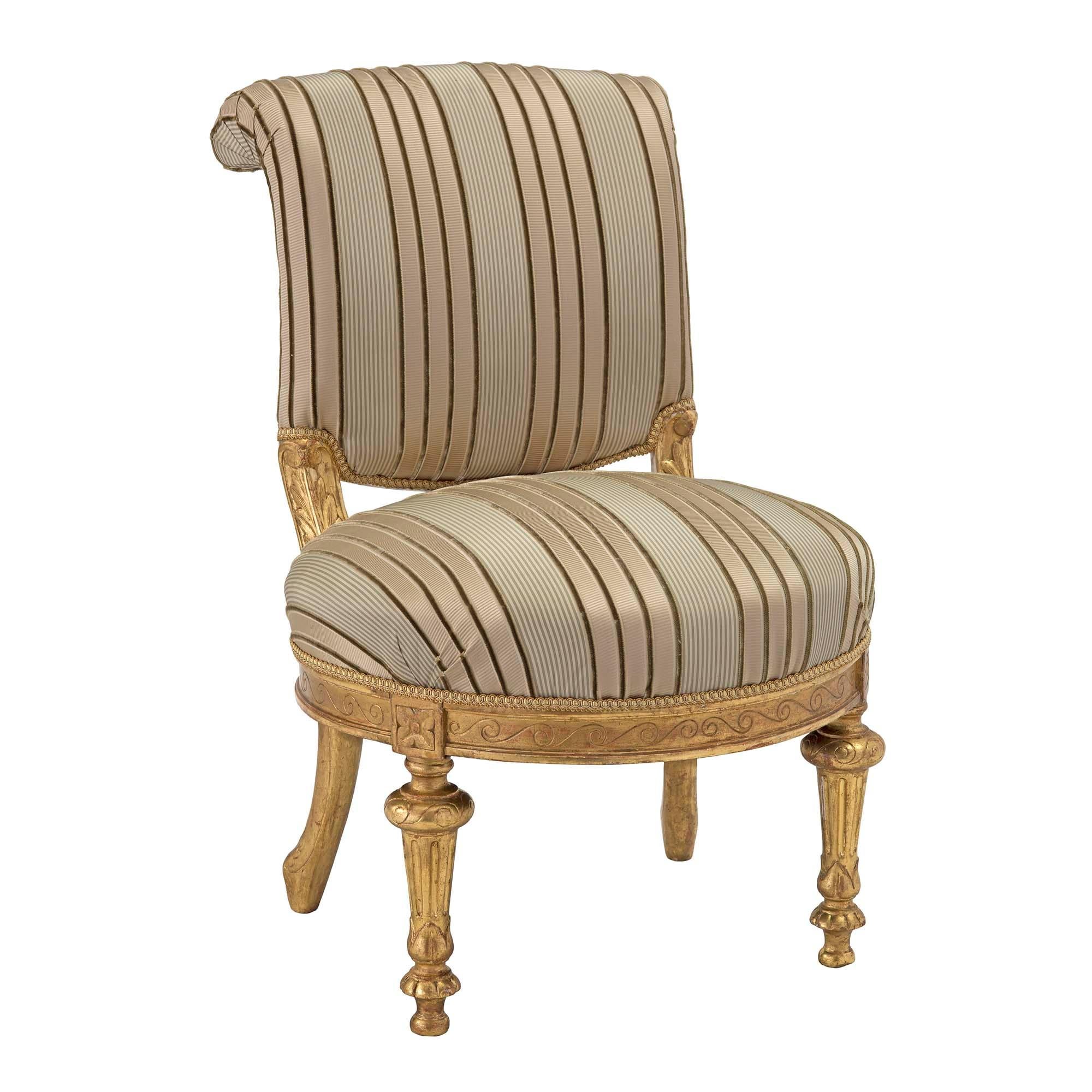A charming Italian early 19th century Louis XVI st. giltwood slipper chair. The chair is raised by two topie shaped feet below circular fluted legs with finely carved top caps at the front and elegant lightly curved legs to the rear. Above each legs