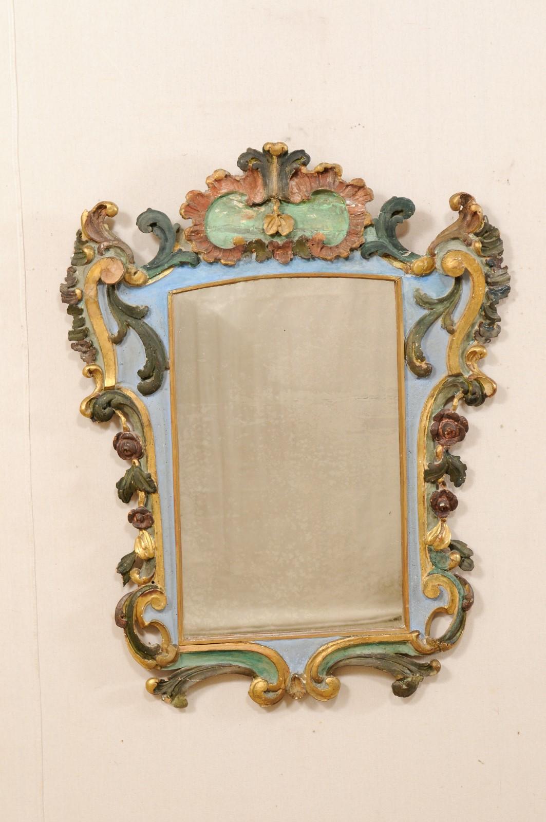 An Italian carved wood mirror with it's original painted finish from the early 19th century. This antique Rococo style mirror from Italy features and elaborately carved surround comprised of delicate florals, elongated scrolls, and acanthus leaf