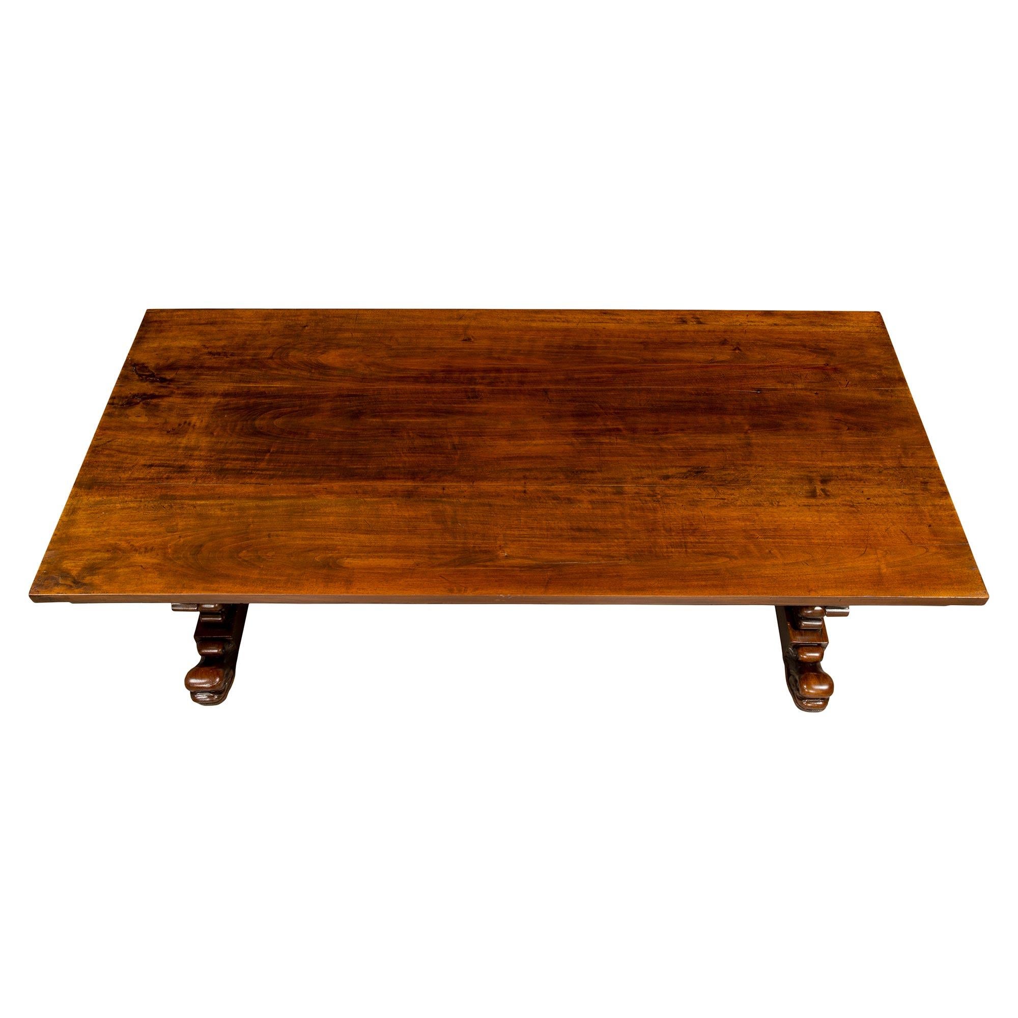 A very handsome Italian early 19th century solid walnut dining table. The table is raised on impressive supports with intricate carvings of large scrolls and acanthus leaves ending with carved dolphins at the base and also at the feet. The supports