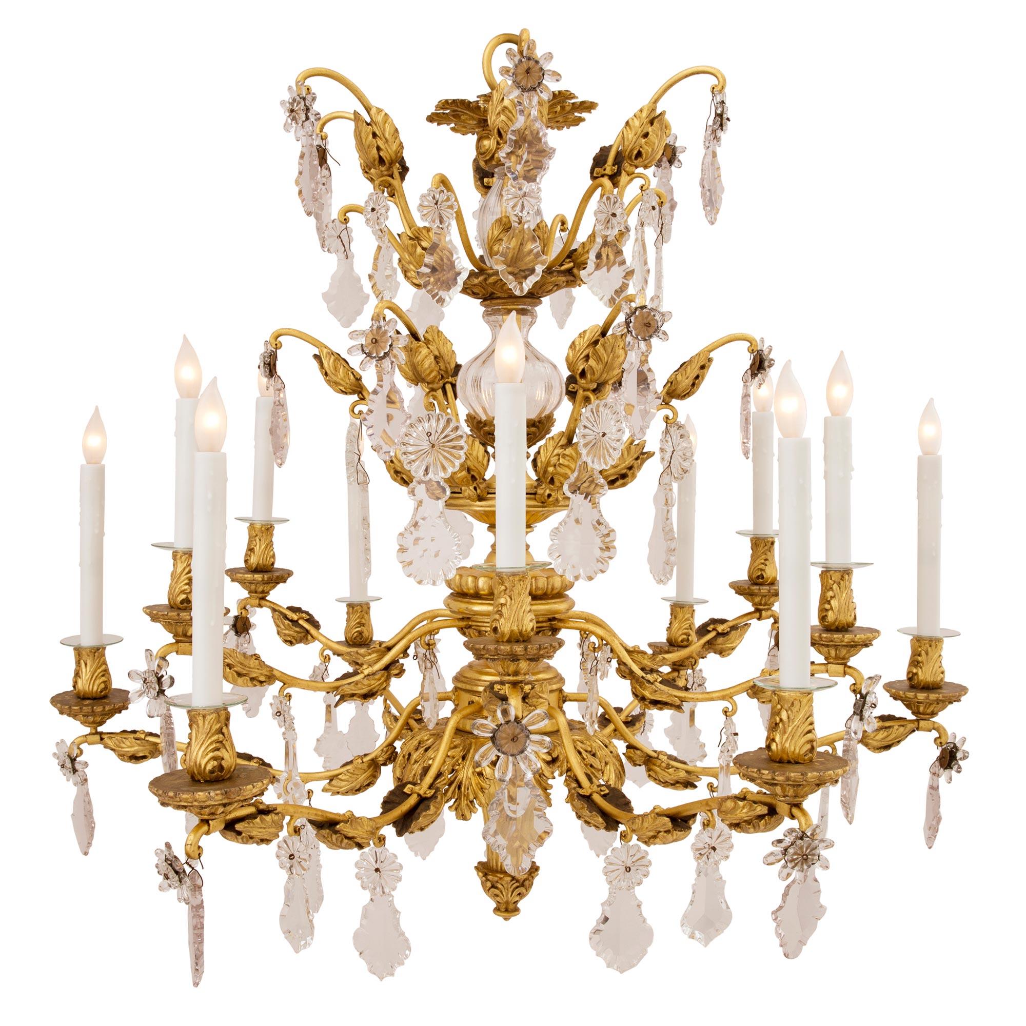 A stunning Italian early 19th century Tuscan giltwood, gilt metal and crystal twelve arm chandelier. The chandelier is centered by a beautiful bottom foliate finial with an elegant tapered spray shaped design. The twelve arms are spread over two
