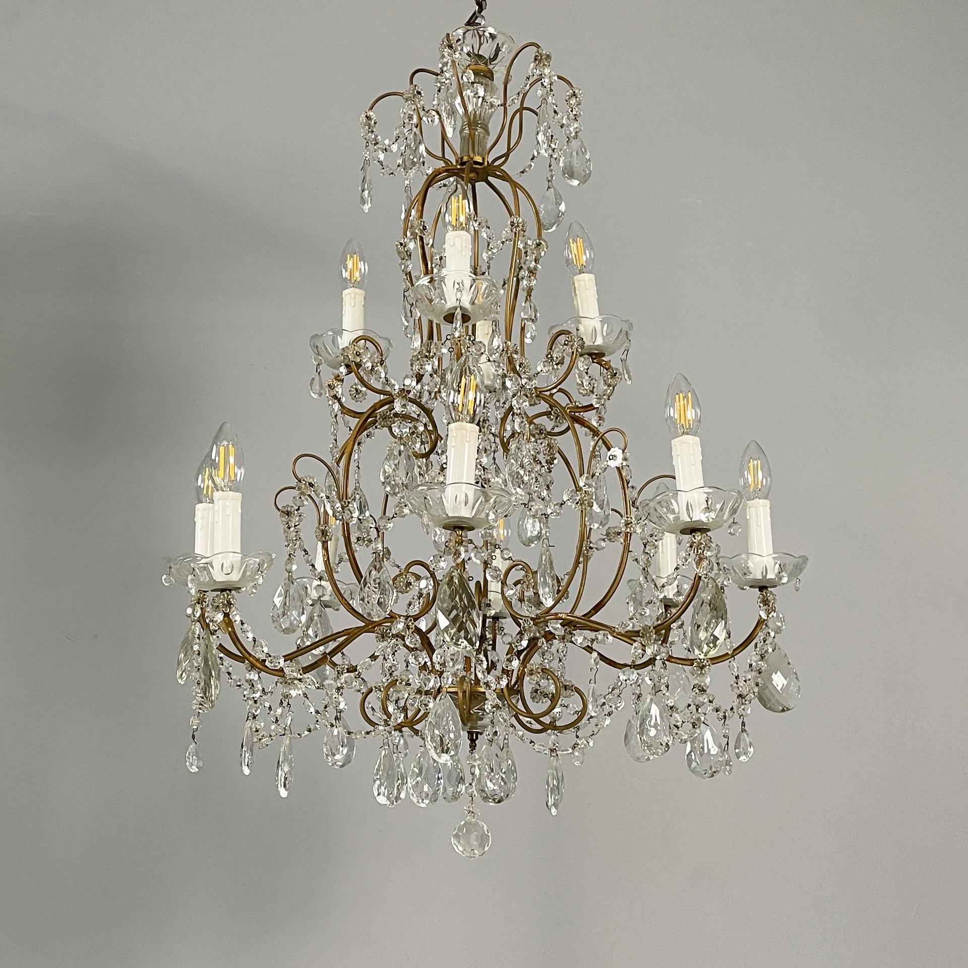 Lustre italien du début du 20e siècle en verre avec structure en laiton, 1900-1950
Lustre en forme de goutte avec douze lumières en forme de bougie, divisé en deux niveaux. La structure est composée de plusieurs tiges de laiton courbées. Des gouttes